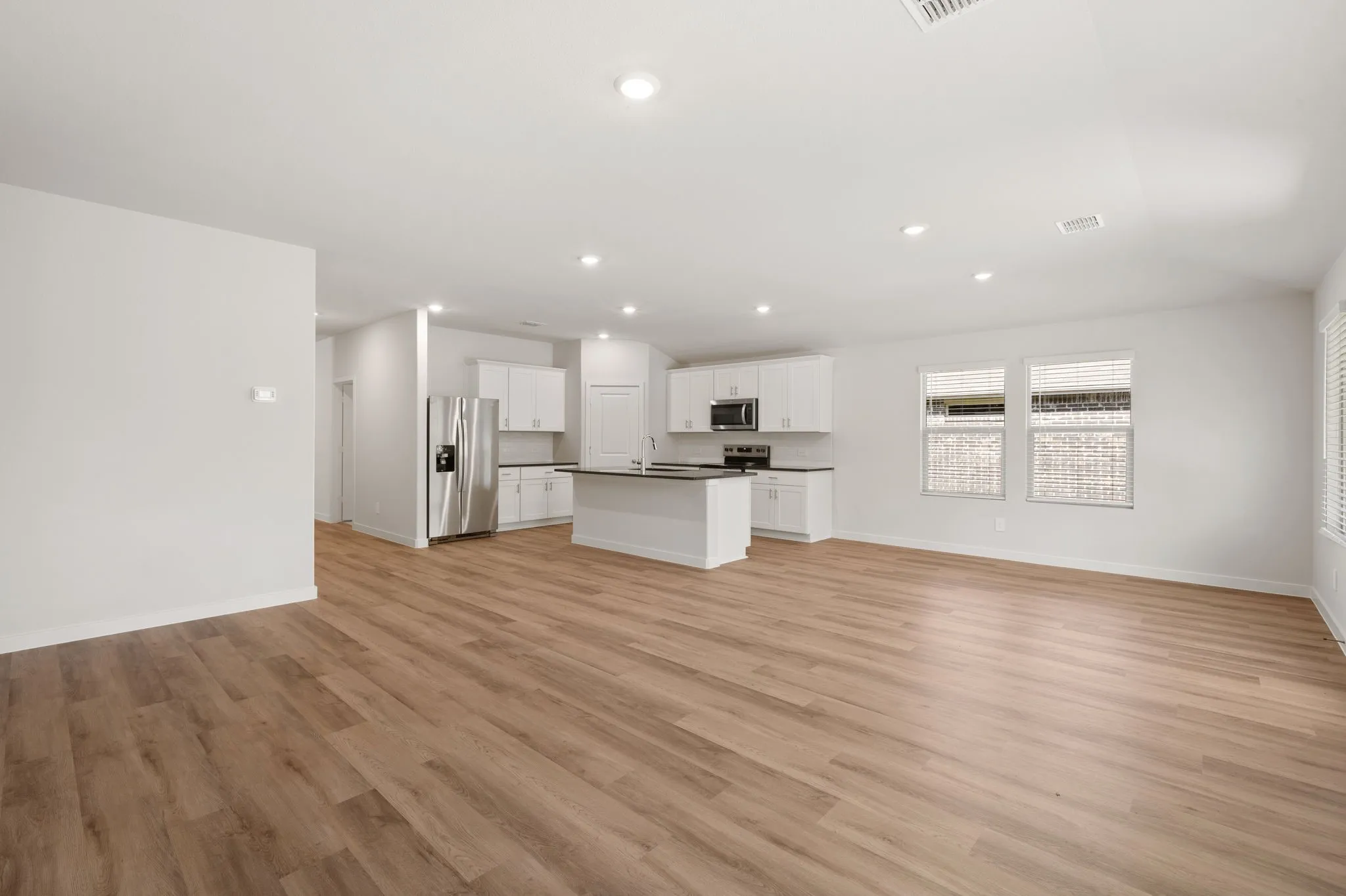 Expansive main living area featuring wood-finish flooring, recessed lighting, and a white kitchen with dark countertops