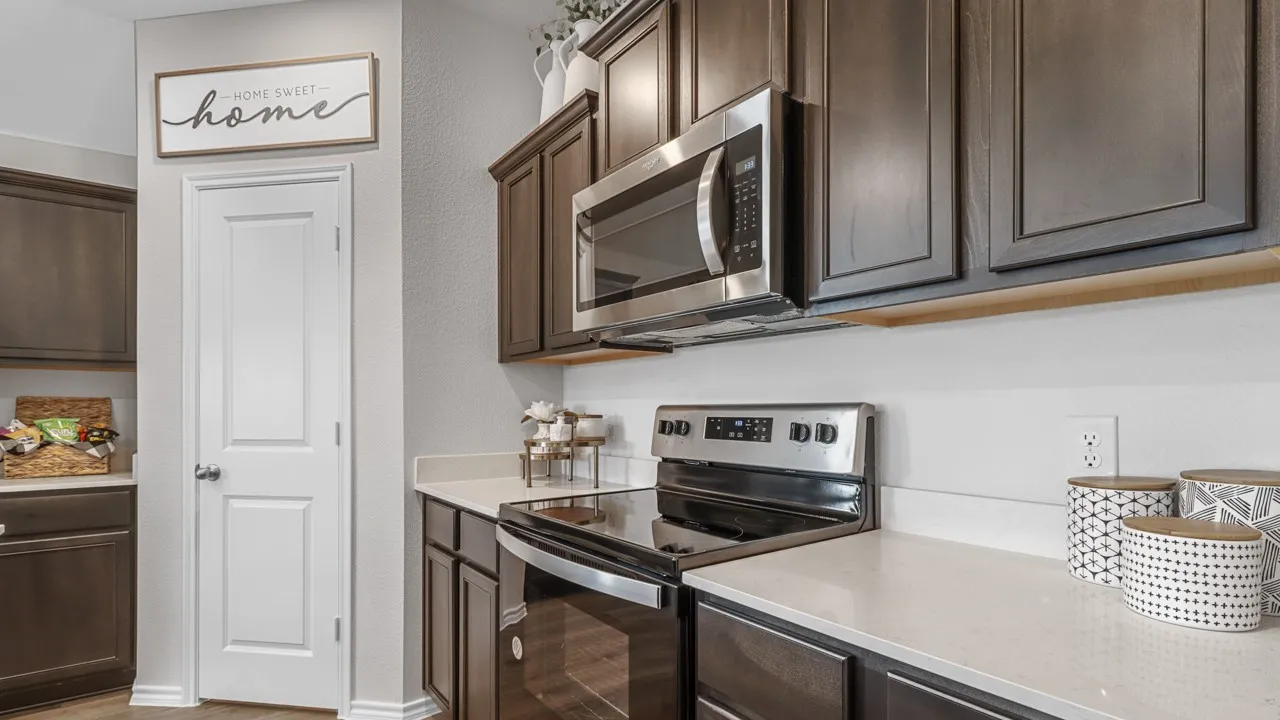 Contemporary kitchen featuring dark wood cabinetry, light-toned countertops, and a full suite of stainless steel appliances including a built-in microwave and electric range