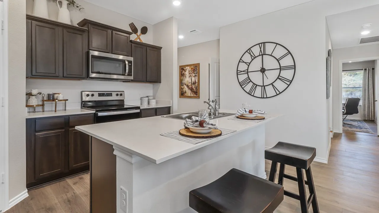 Modern kitchen featuring dark wood-finish cabinetry, stainless steel appliances, a white tile backsplash, and a kitchen island with a light-toned countertop