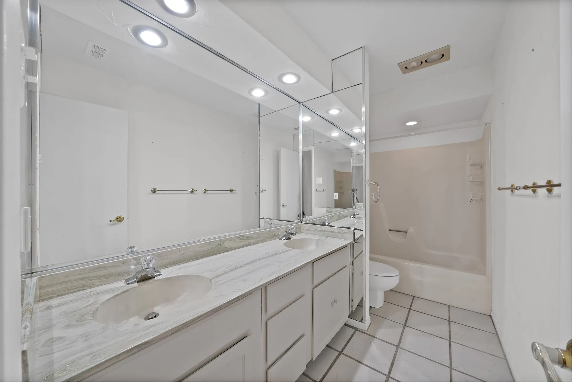 Bathroom featuring a dual-sink vanity with a stone countertop, white cabinetry, and an integrated mirror with overhead lighting