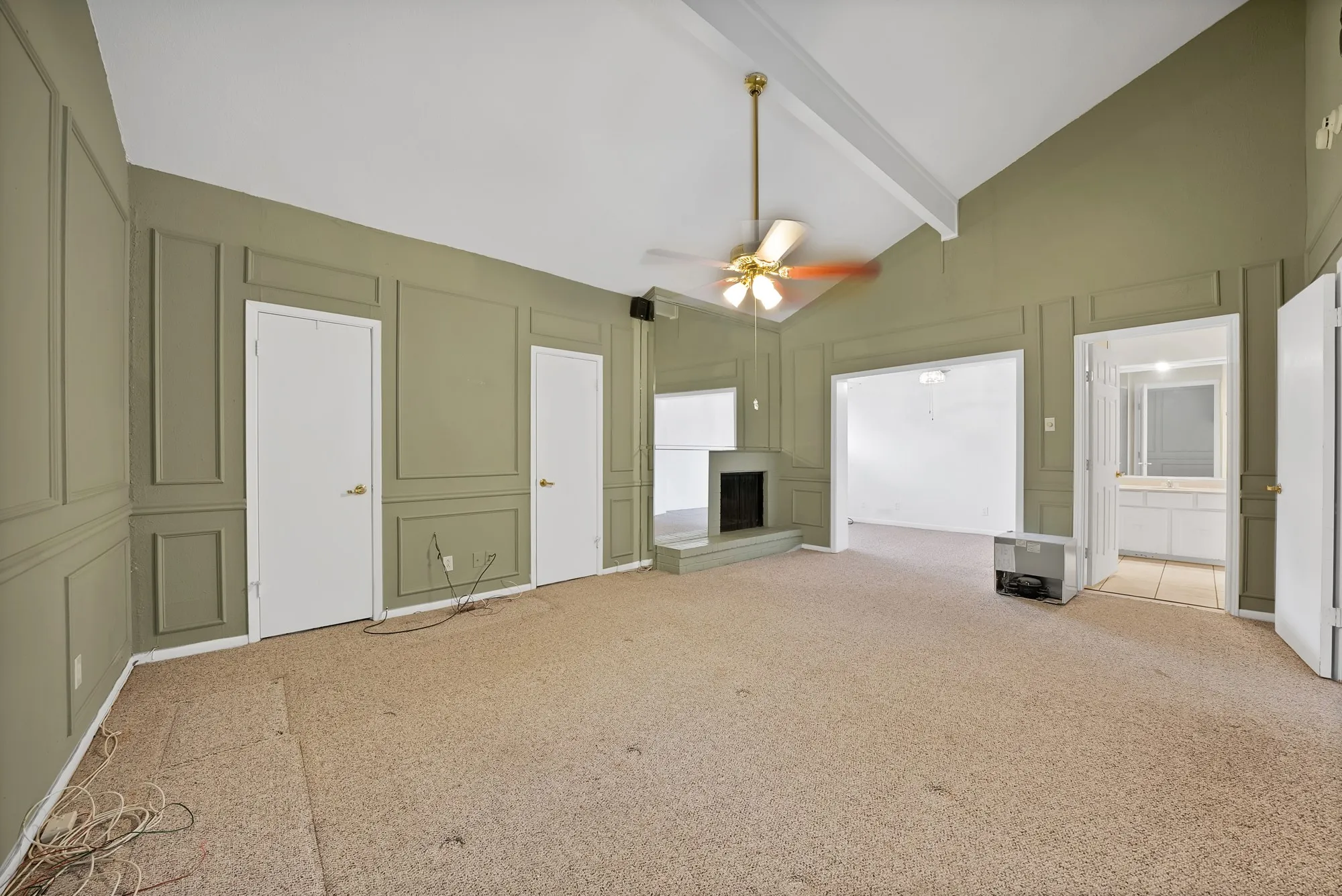 Spacious living area featuring a vaulted ceiling with exposed beams, decorative wall paneling, and a corner fireplace