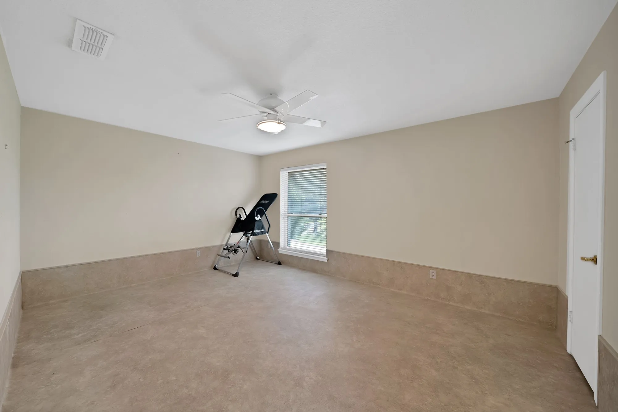 Spacious room featuring neutral-toned walls, a ceiling fan with integrated lighting, a window with blinds, and durable flooring