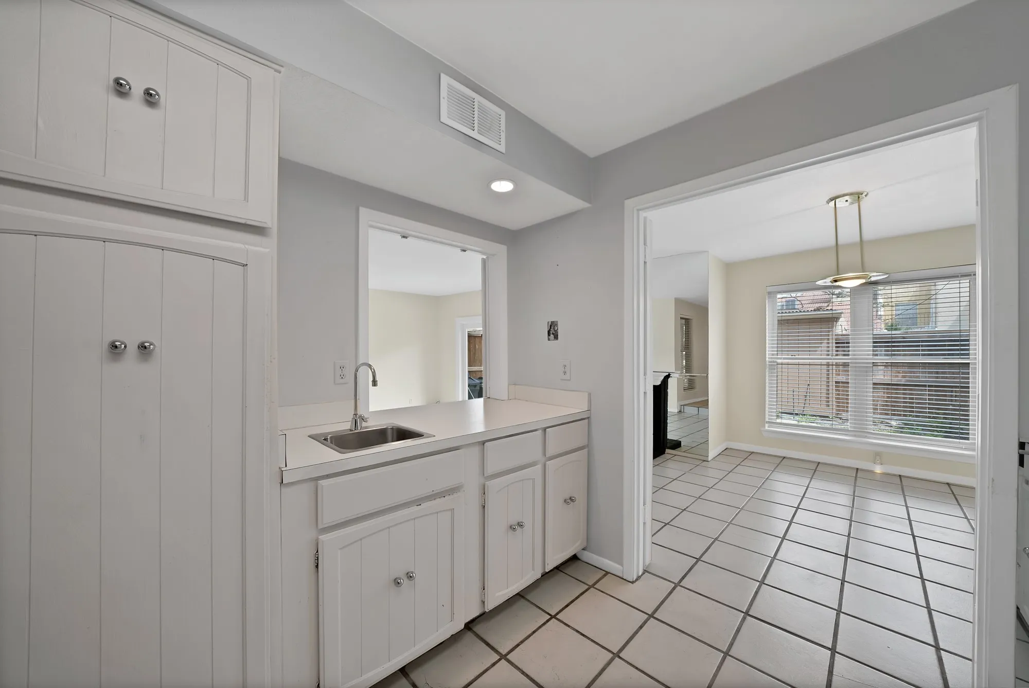 Kitchenette featuring a stainless steel sink with a gooseneck faucet, white cabinetry, and light-toned countertops