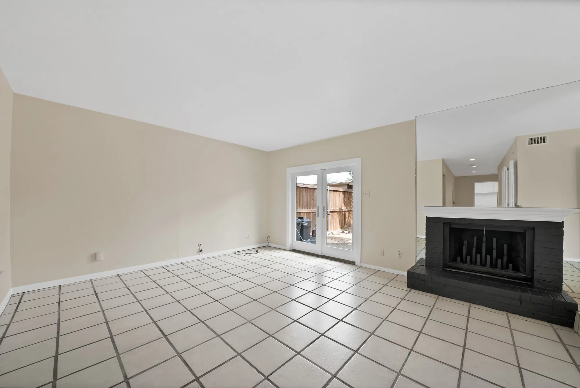 Spacious room with large ceramic tile flooring, a prominent black brick fireplace with a white mantel, and mirrored wall accents