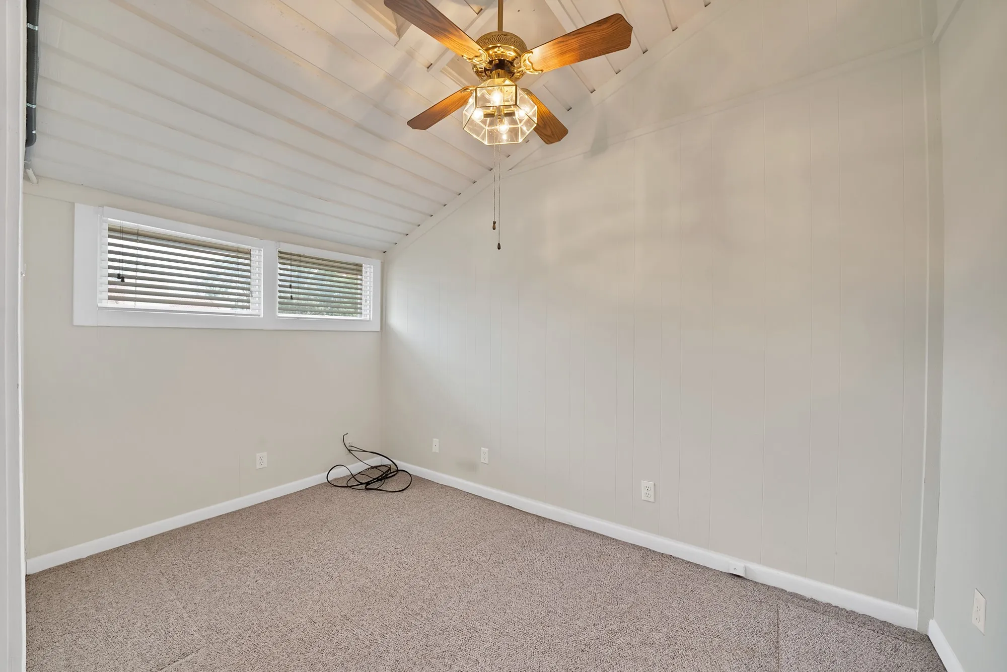 Room featuring a vaulted ceiling with exposed white wood planks, a ceiling fan with integrated lighting, and a neutral-toned carpeted floor