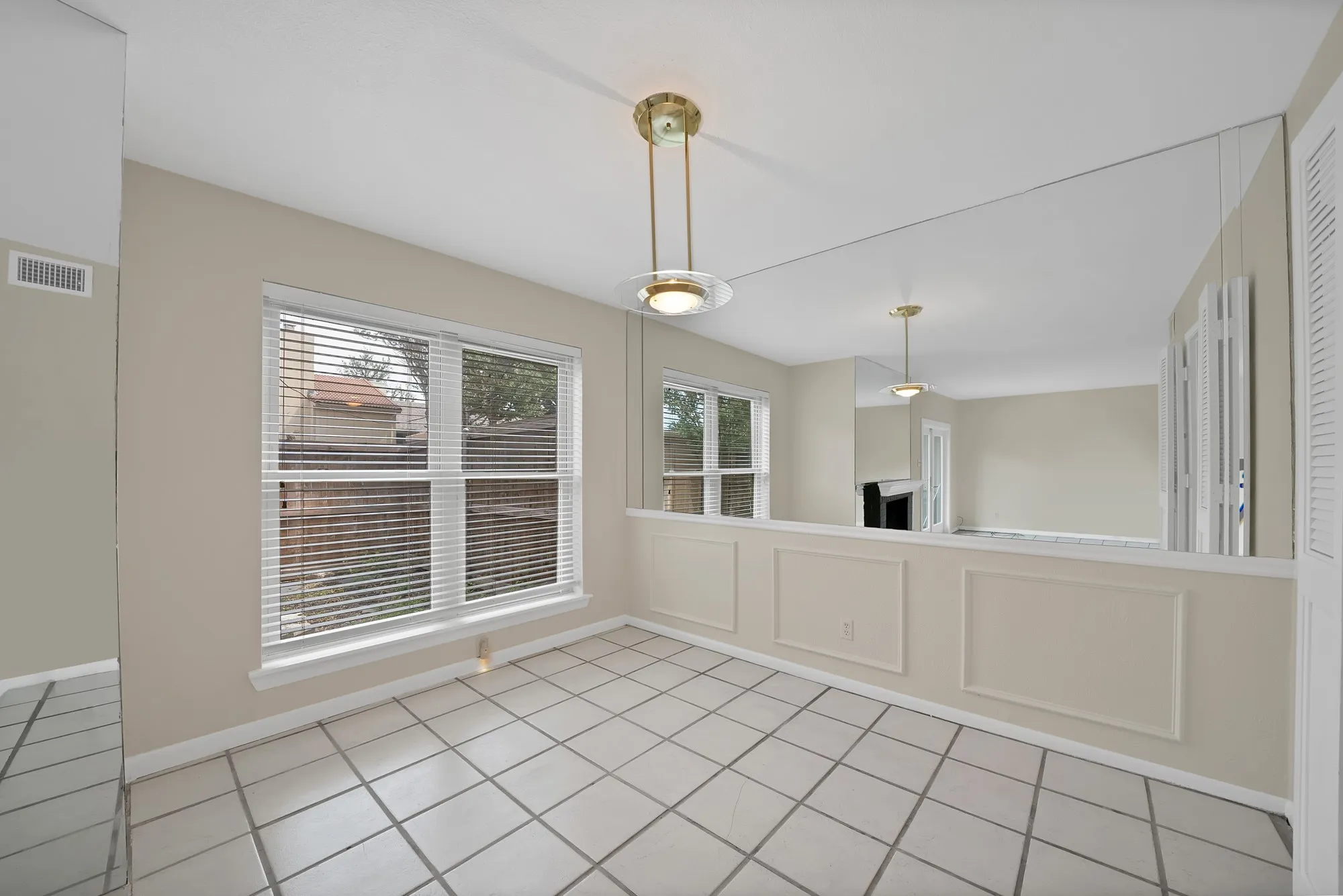 Dining area featuring large window with blinds, overhead lighting fixture, tiled flooring, and a mirrored wall panel