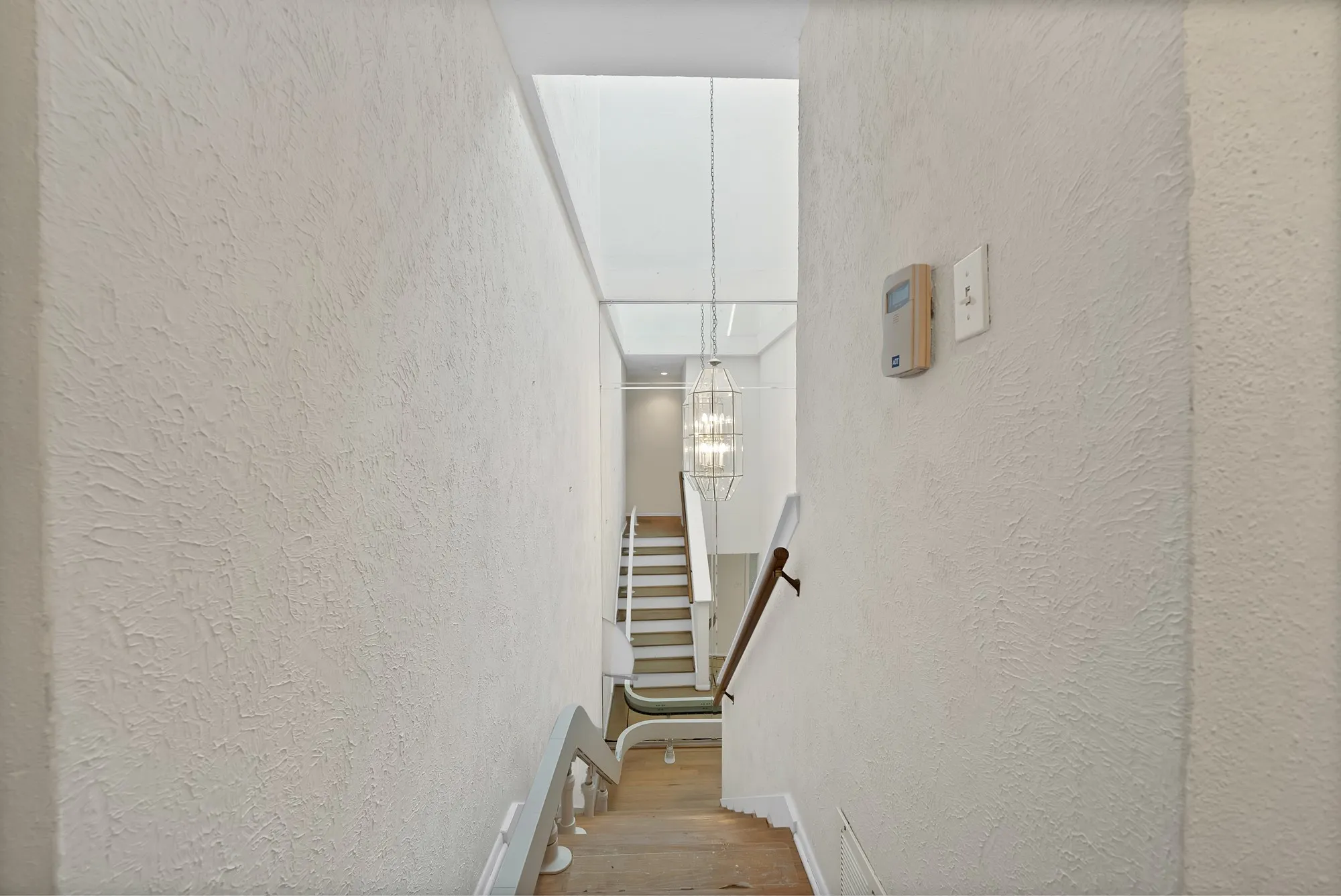 Stairwell featuring wood-finish flooring, white risers, and a contemporary chandelier
