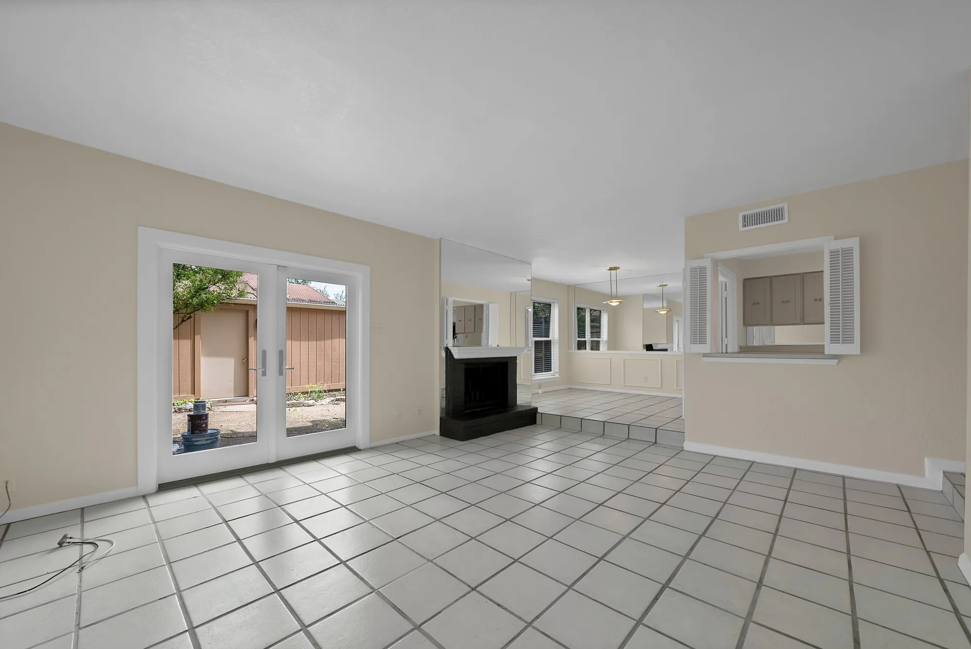Spacious interior featuring light-colored tile flooring, a black hearth and fireplace, and white-framed glass French doors