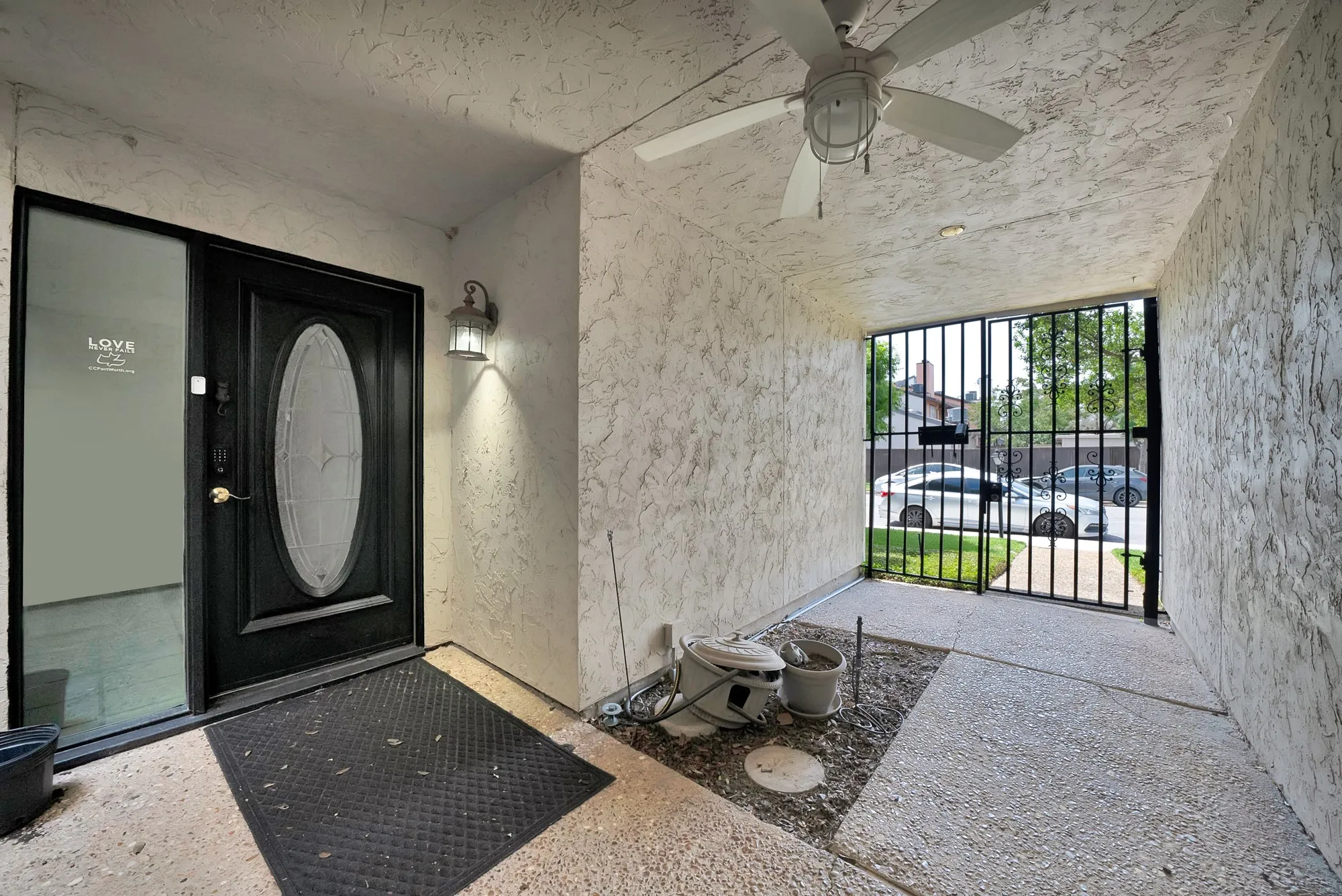 Covered entryway featuring a black front door with an oval glass insert, an attached exterior light fixture, and a ceiling fan