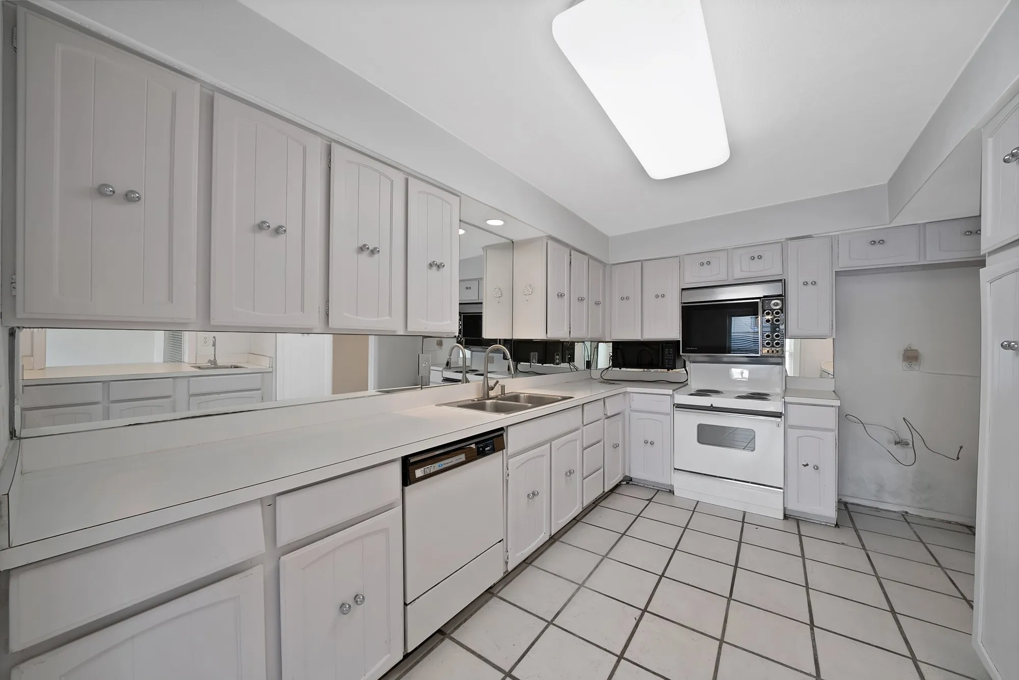 Kitchen featuring white cabinetry, integrated appliances, mirrored backsplash, laminate countertops, and tile flooring