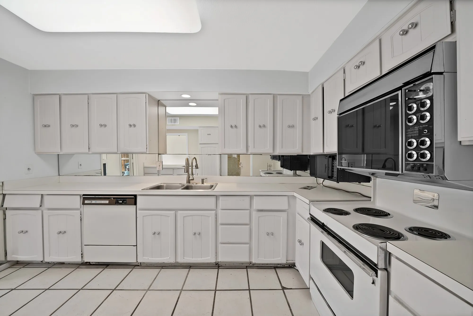 Kitchen featuring white cabinetry with silver hardware, a white solid surface countertop, an undermount double basin sink with a gooseneck faucet, a built-in dishwasher, and an electric range with an overhead microwave
