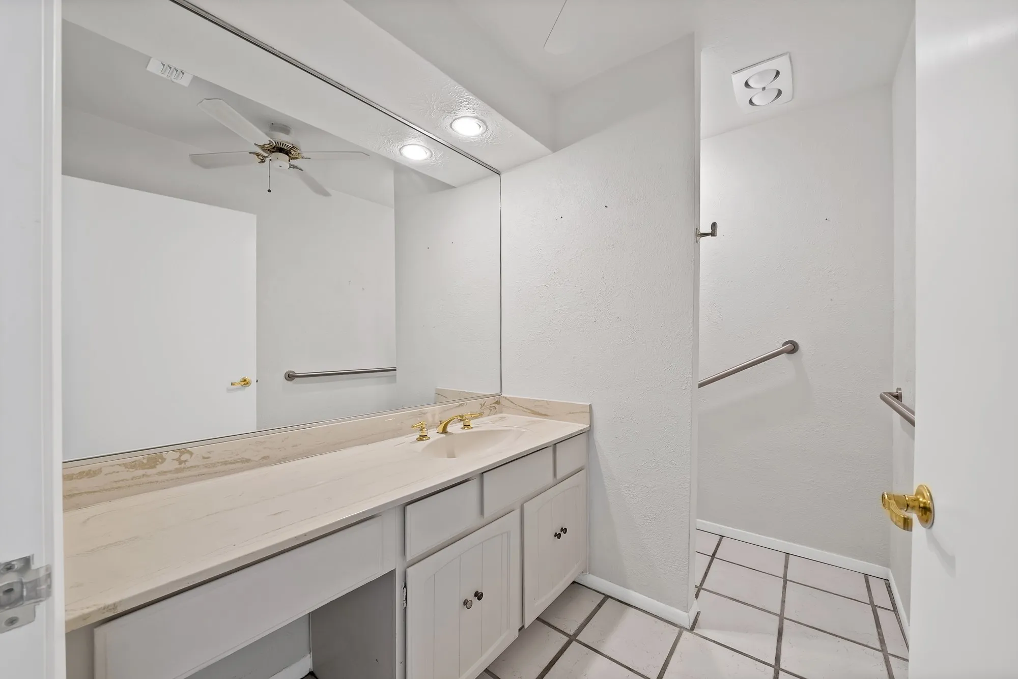 Bathroom vanity featuring a light-toned countertop, undermount sink, and brass-finish faucet