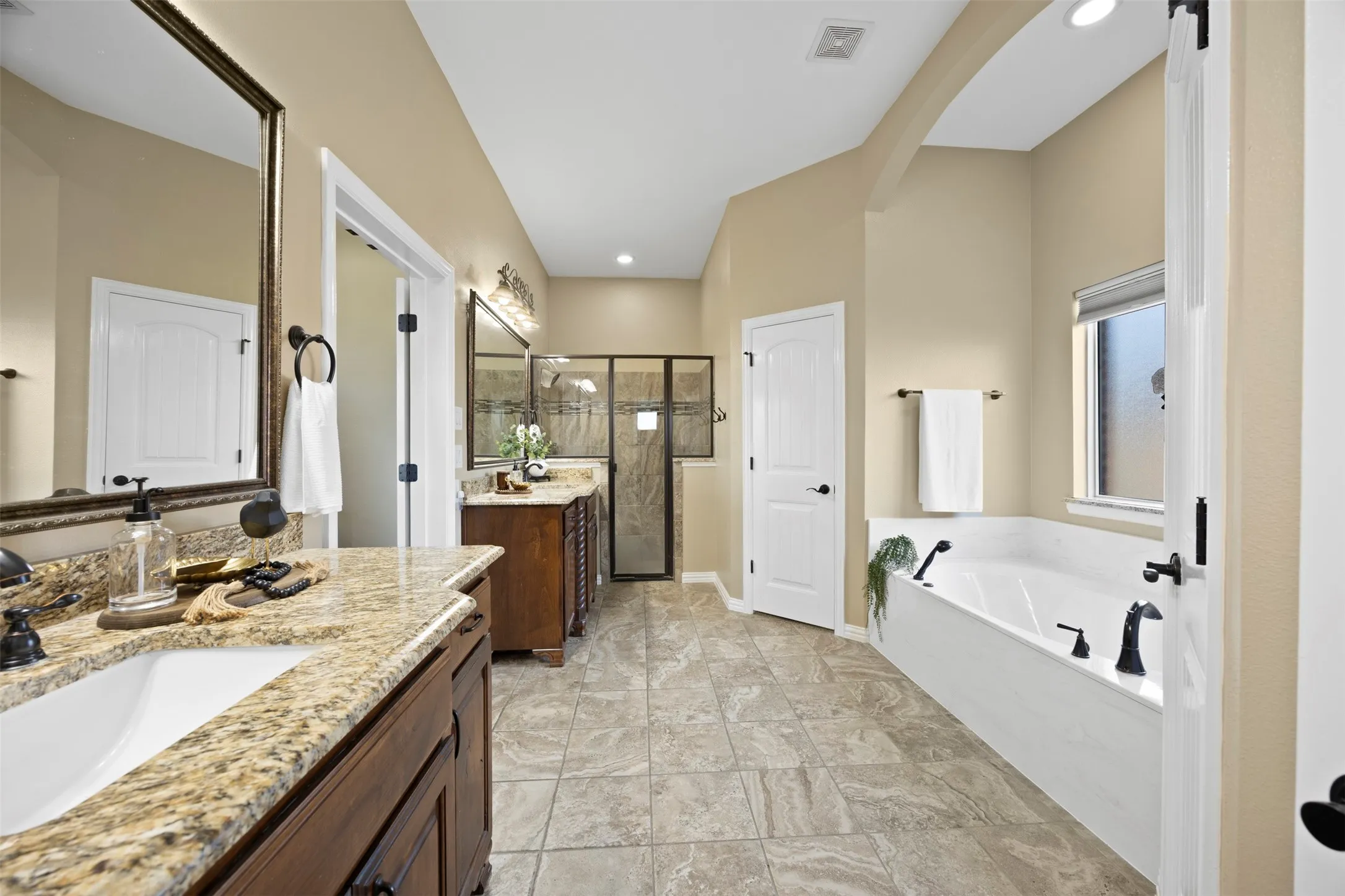 Bathroom featuring a dual vanity with granite countertops, wood cabinetry, and a framed mirror