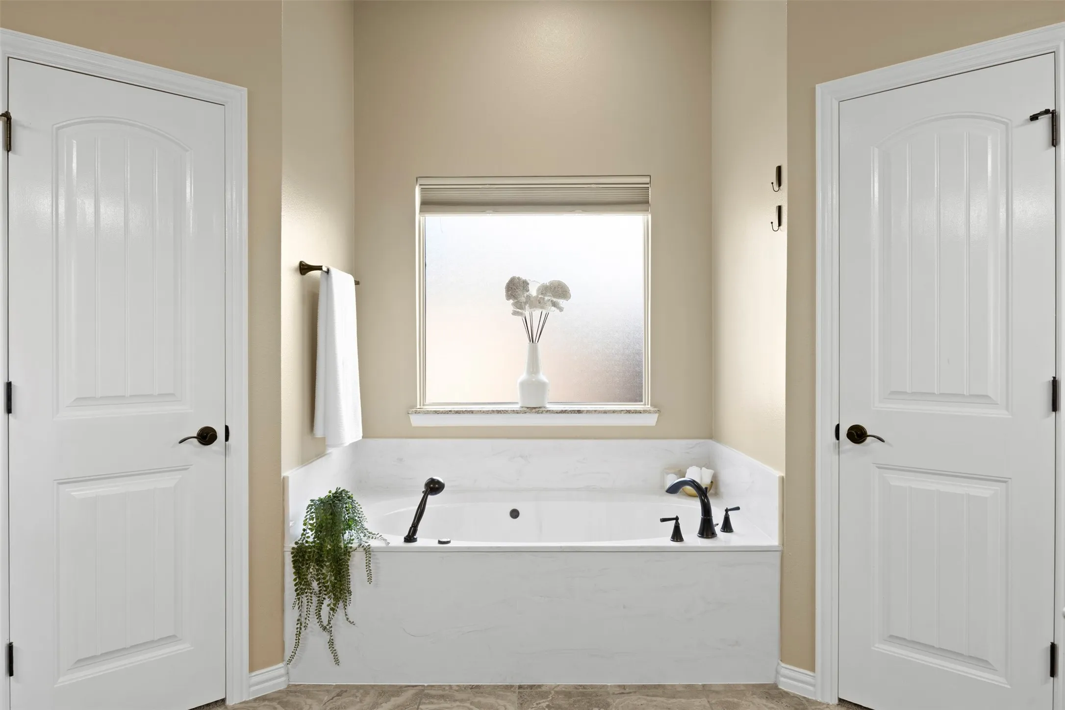 Built-in soaking tub with a dark bronze faucet, surrounded by marble-finish tile and a granite-finish window sill