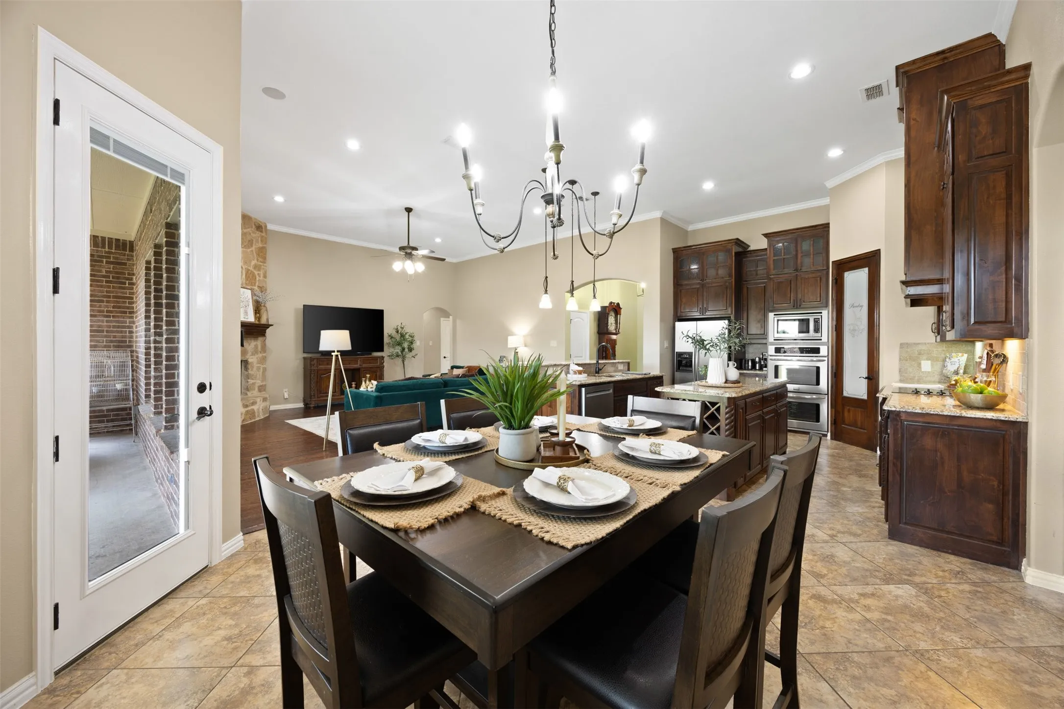 Open-concept living space featuring a dining area with tile flooring, an ornate chandelier, and a white glass-paneled door