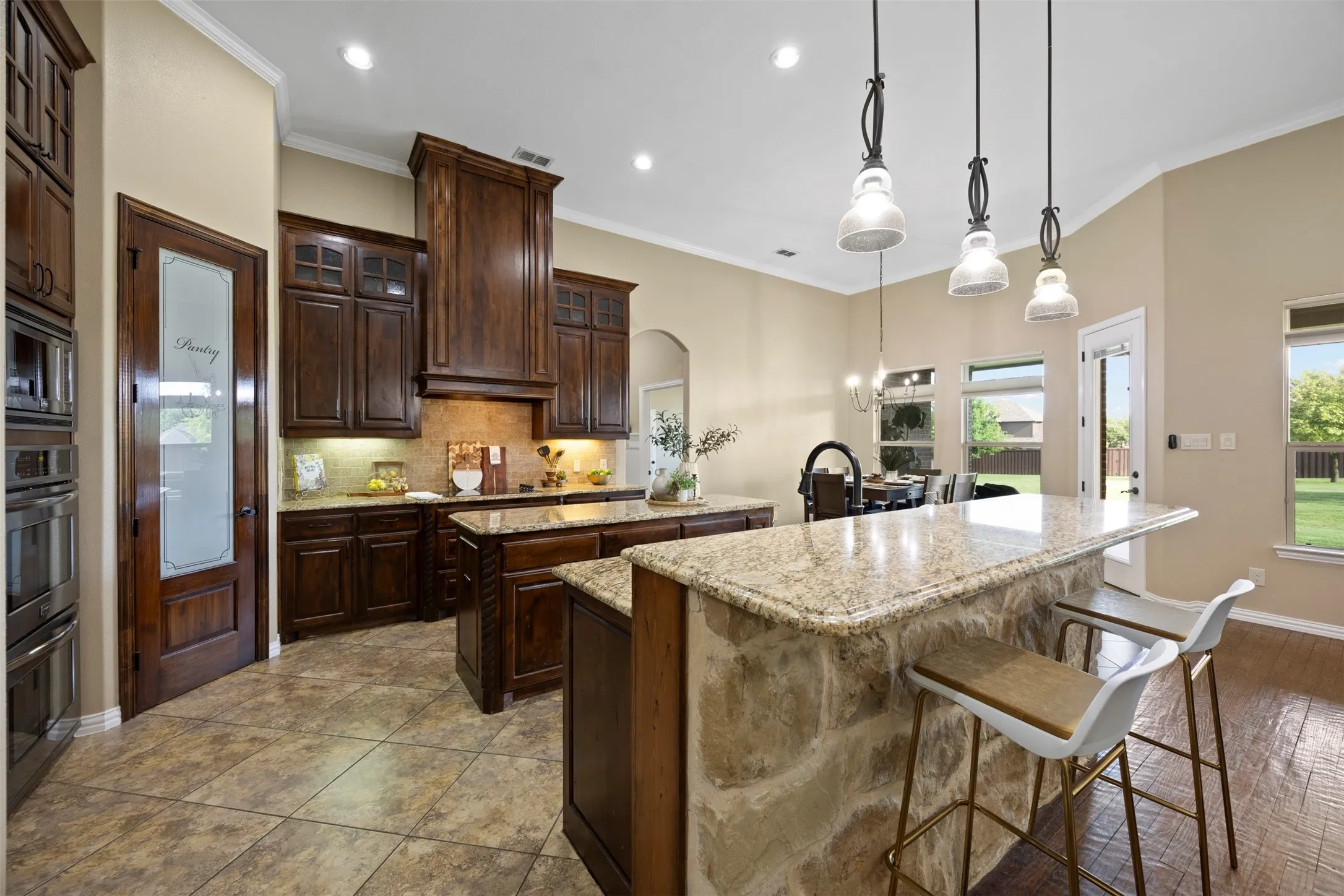 Kitchen featuring dark wood cabinetry, granite countertops, two kitchen islands, tile flooring, and integrated stainless steel appliances