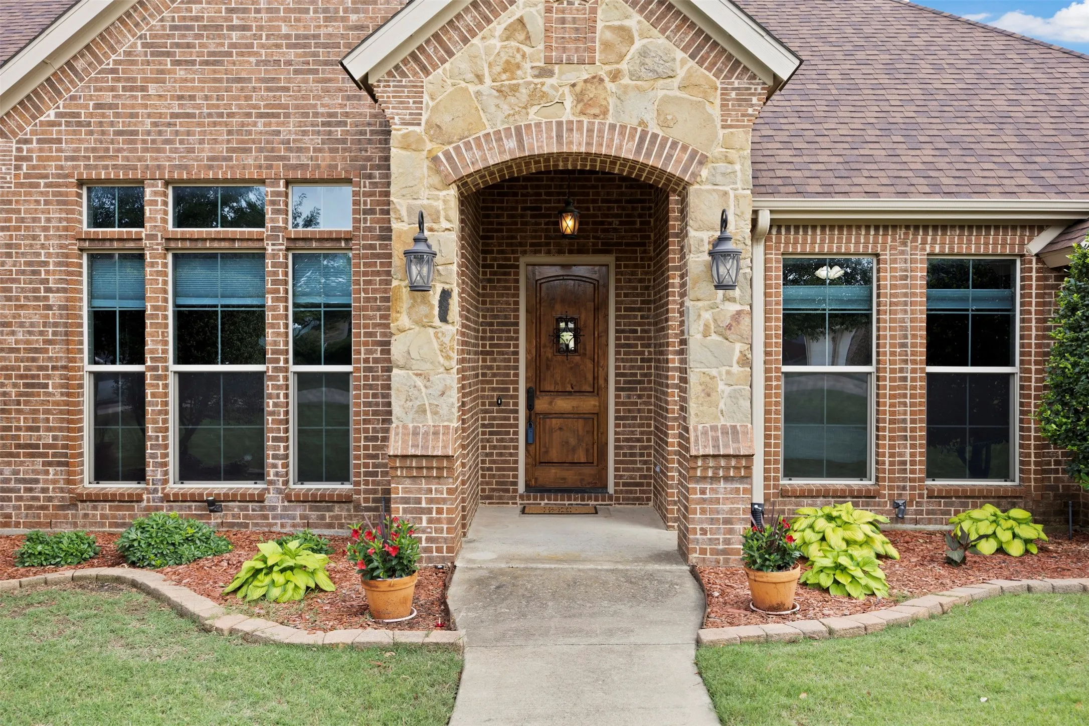 Brick and stone facade featuring an arched entryway with a wood-finish door