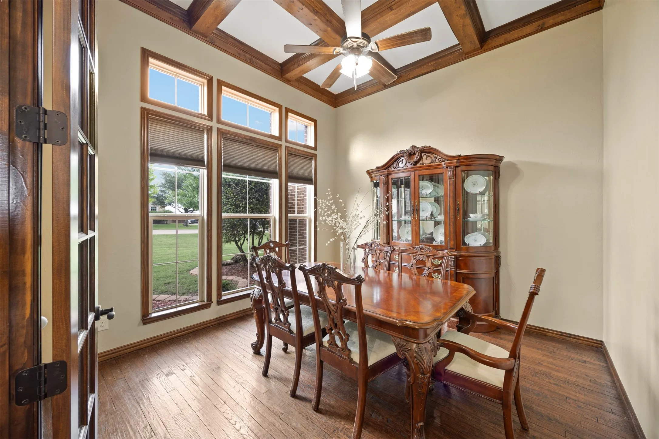 Coffered ceiling with exposed wood beams, wood-finish flooring, and a wall of windows featuring transom accents