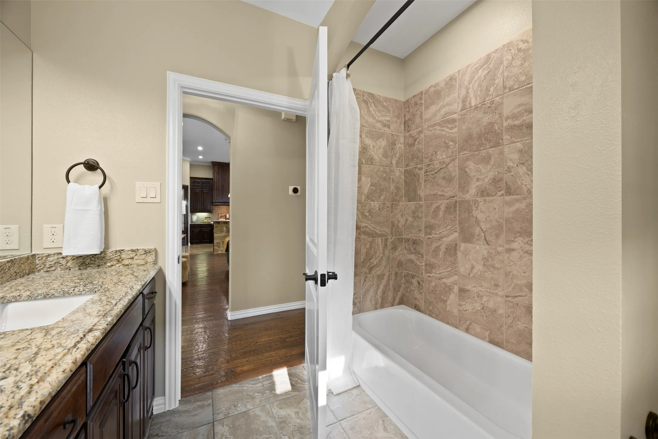 Bathroom featuring a granite countertop vanity with an undermount sink, dark wood cabinetry, and a tub with tiled surround