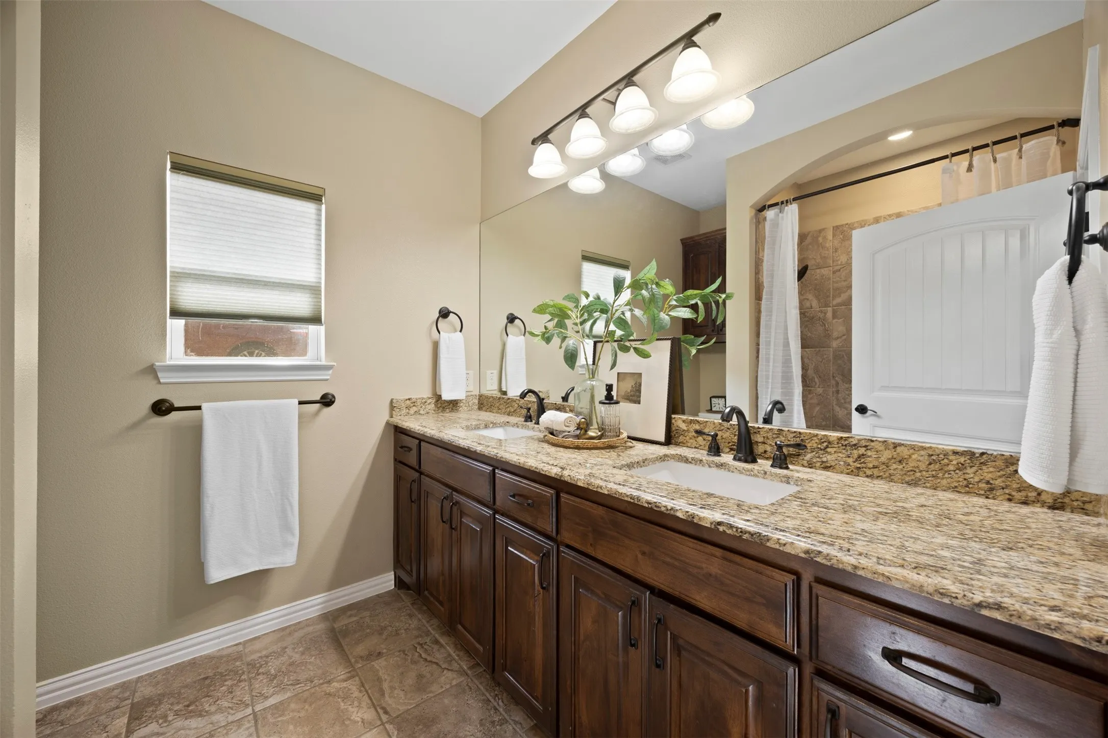 Double vanity featuring a light-toned countertop, dual undermount sinks with oil-rubbed bronze fixtures, and rich wood cabinetry