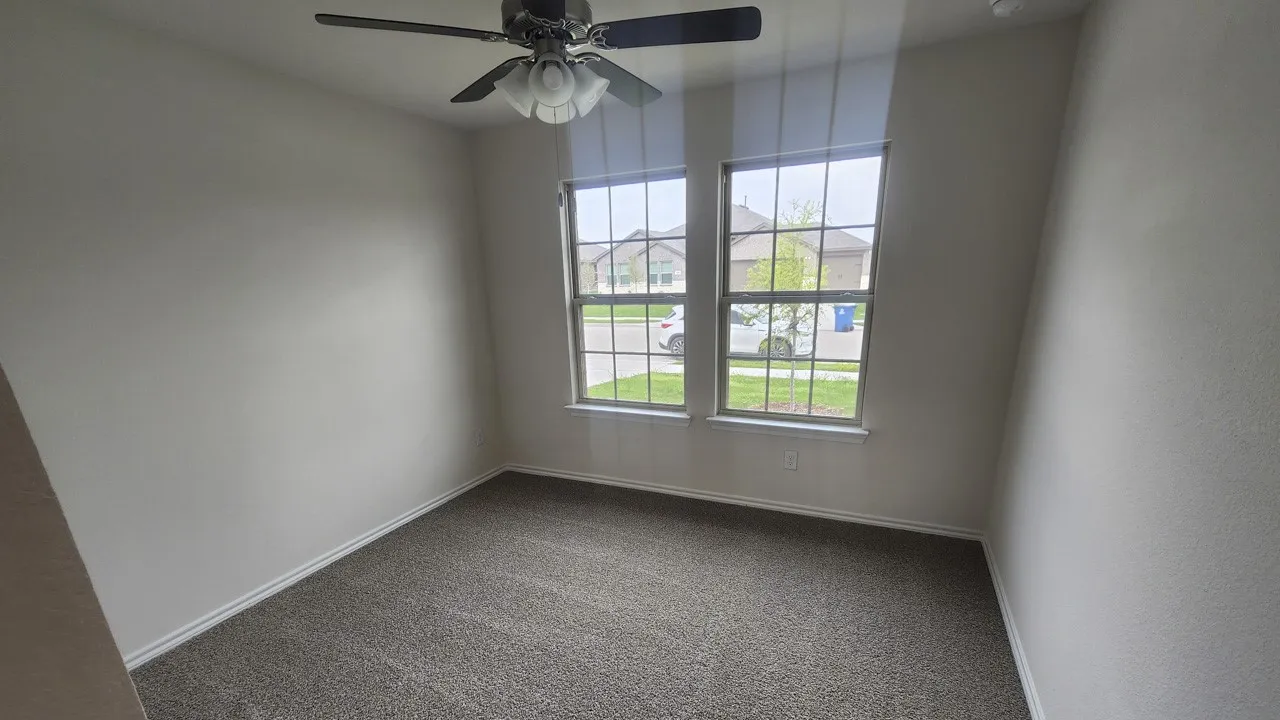 Room featuring two large windows, neutral-toned carpeting, and a ceiling fan with integrated lighting