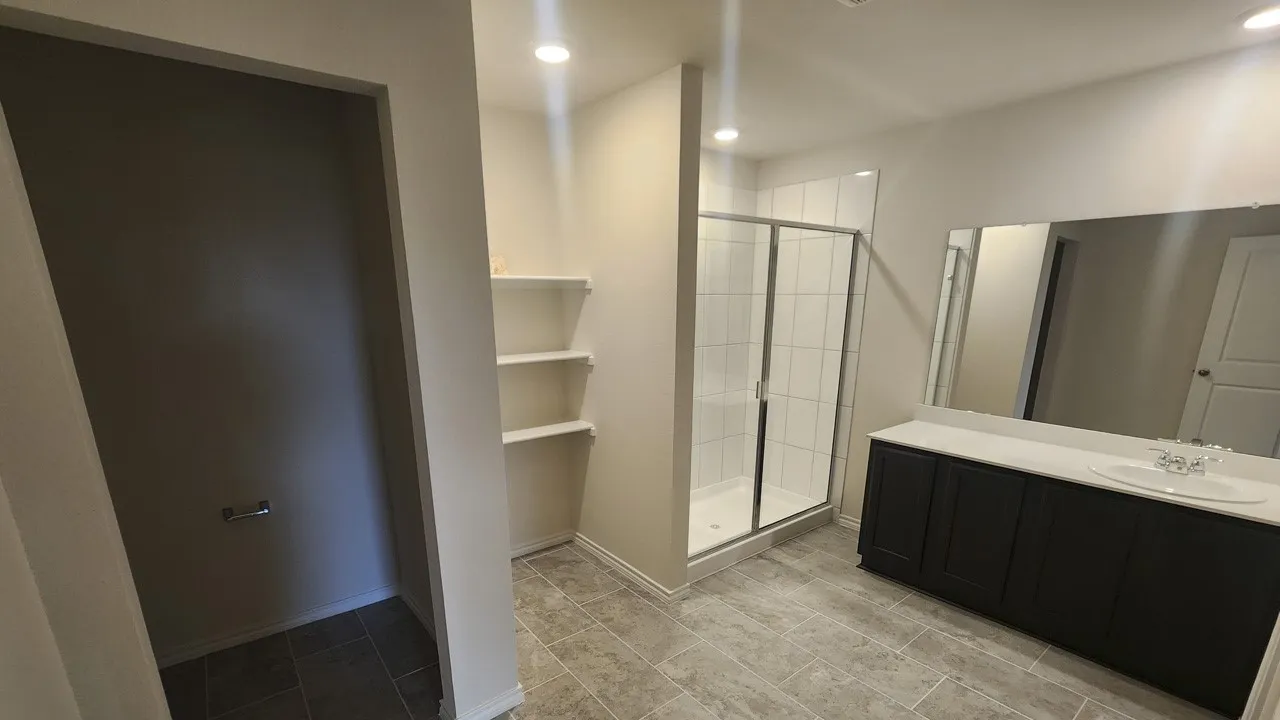 Spacious bathroom featuring a dark wood-finish vanity with an integrated sink, a large wall-mounted mirror, and a glass-enclosed shower with white tiled walls