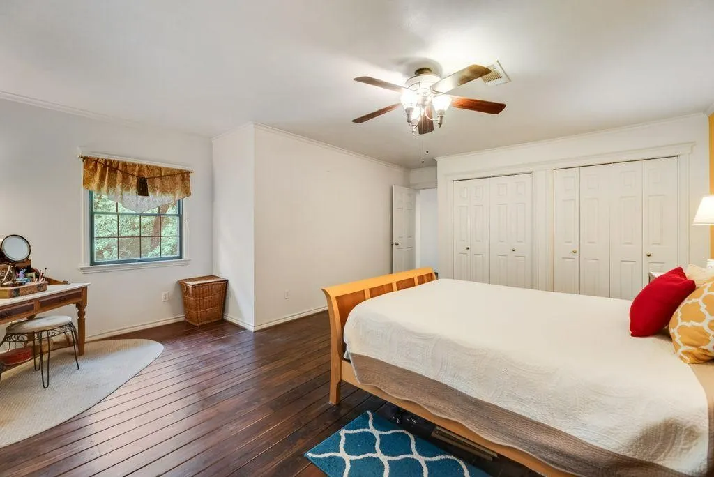 Bedroom featuring wood-finish flooring, a window with exterior tree views, a ceiling fan with integrated lighting, and two sets of bi-fold closet doors