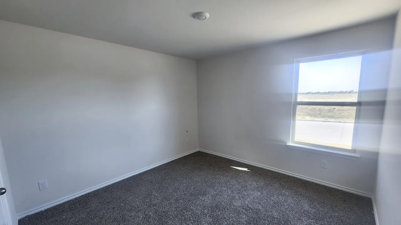 White walls showcasing a single window with a white frame, dark gray textured carpeting, and white baseboards