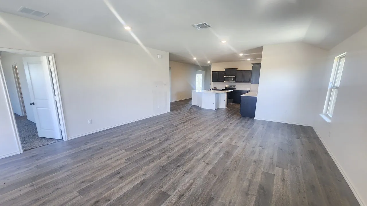 Spacious living area featuring wood-finish flooring, recessed lighting, white walls, and a window for natural illumination