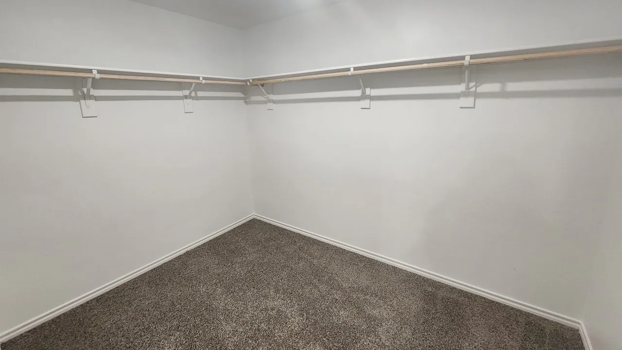 Walk-in closet with neutral-toned carpeting, white baseboards, and built-in wood-finish shelving and hanging rods