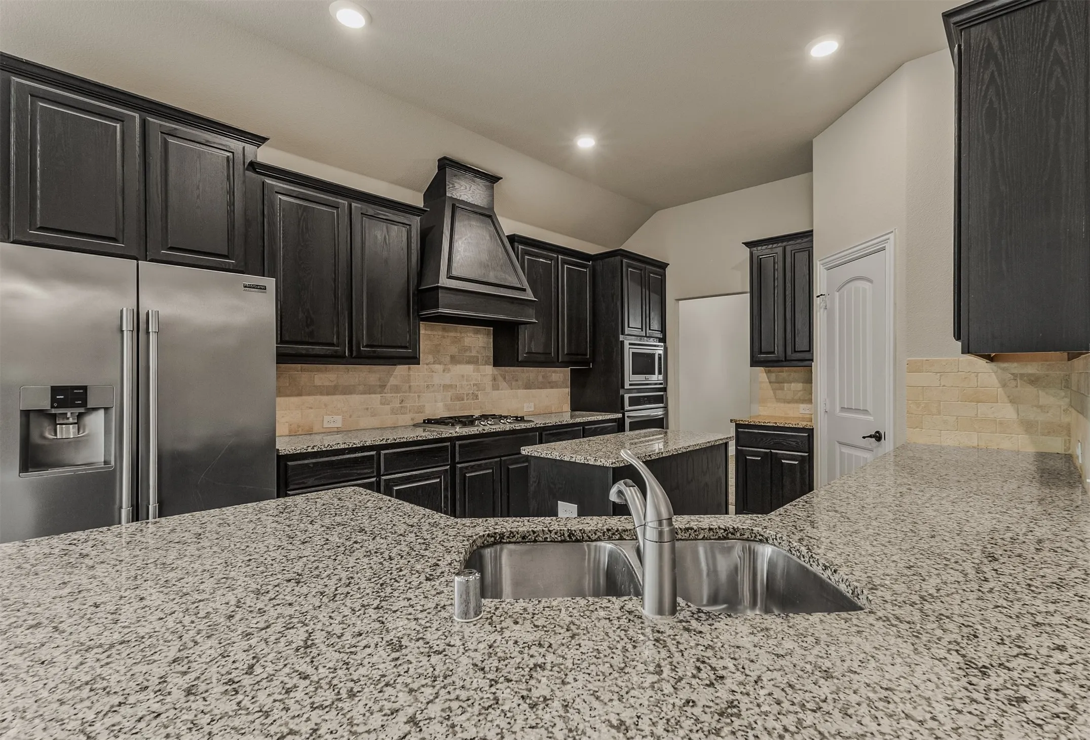 Kitchen featuring granite countertops, dark wood cabinetry, a stainless steel sink, recessed lighting, and a subway tile backsplash