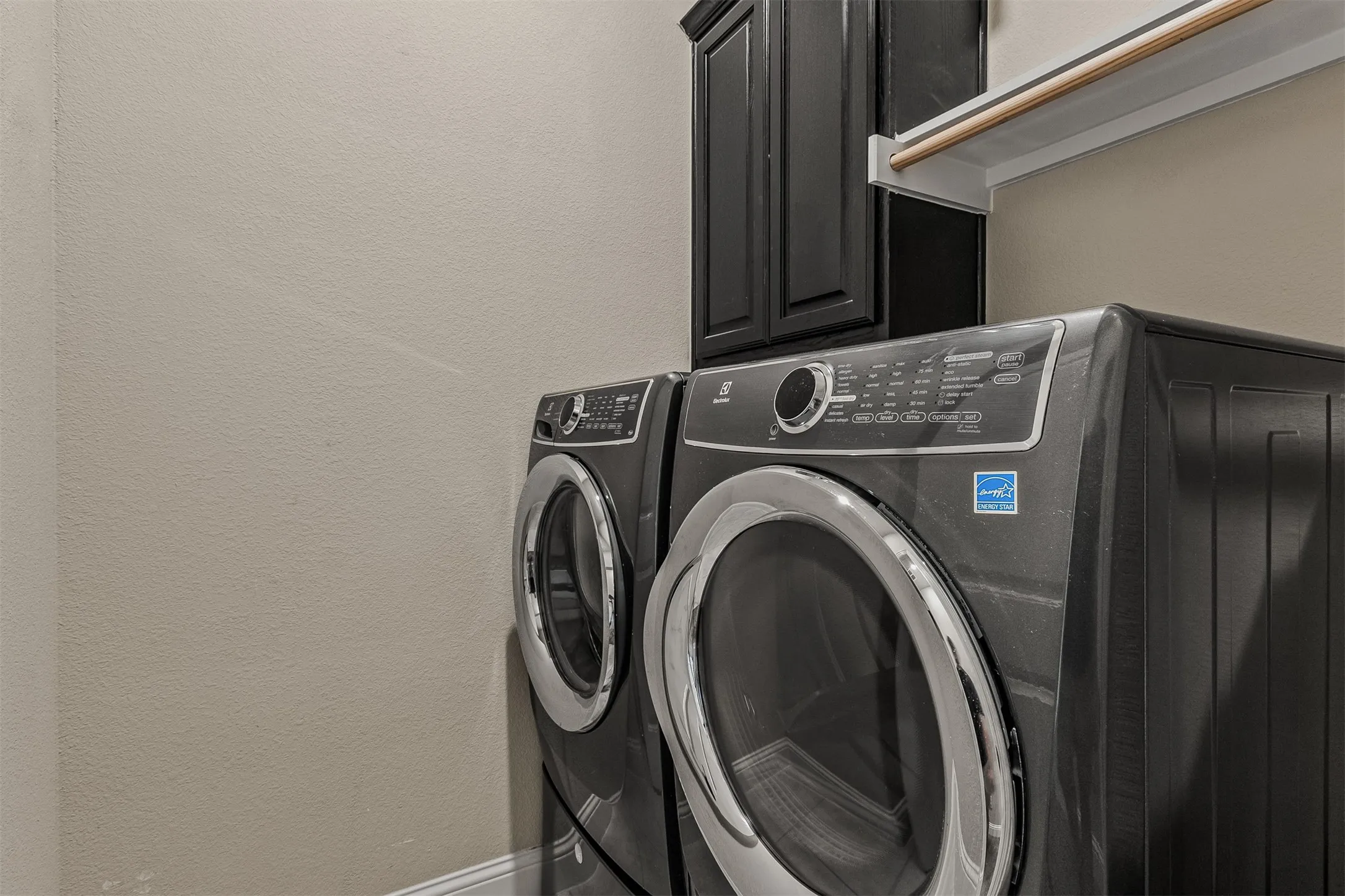 Laundry area featuring a dark cabinetry storage unit, an overhead shelf, and front-loading appliances