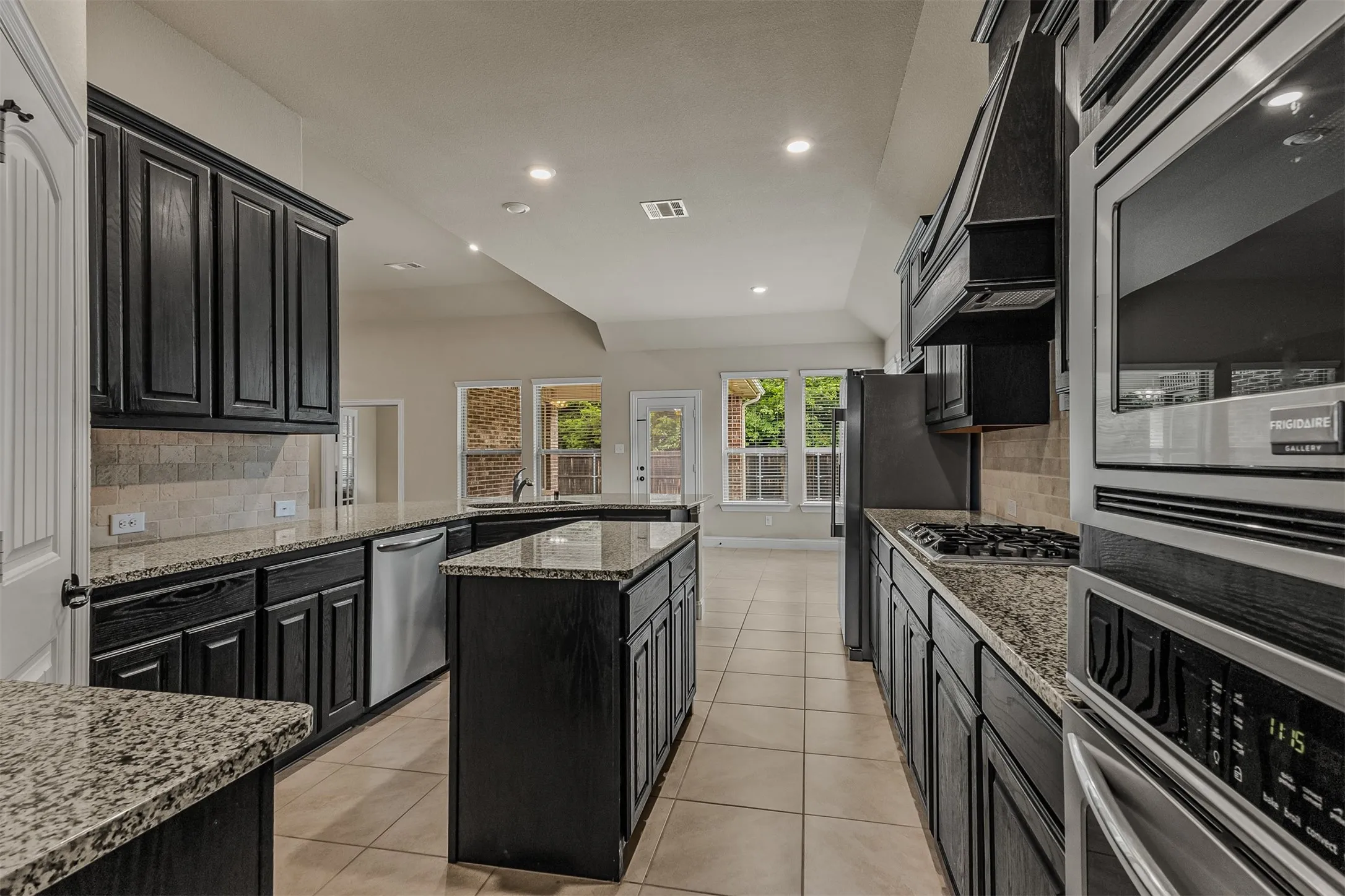 Kitchen featuring dark wood cabinetry, light granite countertops, stainless steel appliances, and a central island