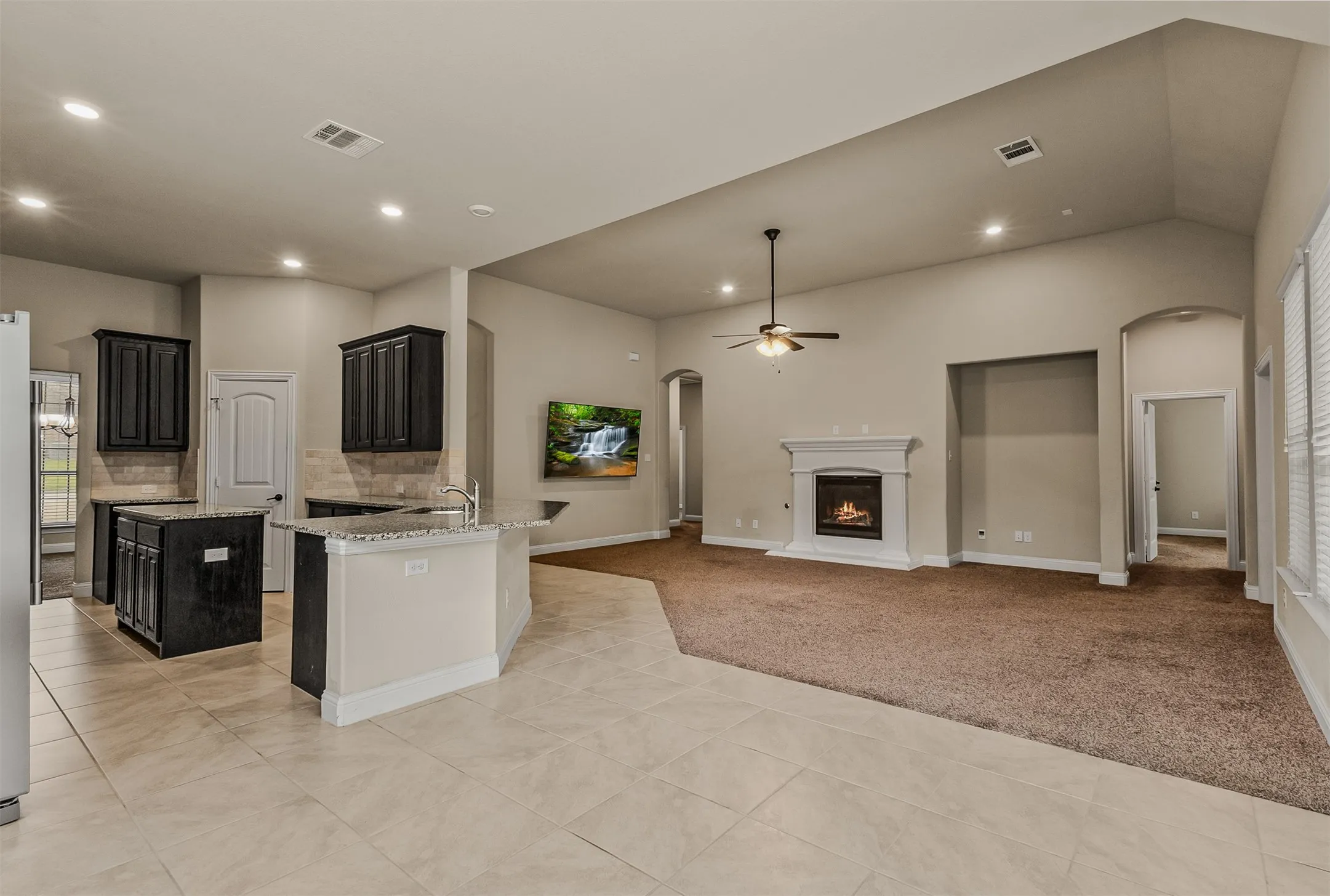 Spacious open-concept living area featuring an inviting fireplace with a white mantle, vaulted ceilings, recessed lighting, and a ceiling fan