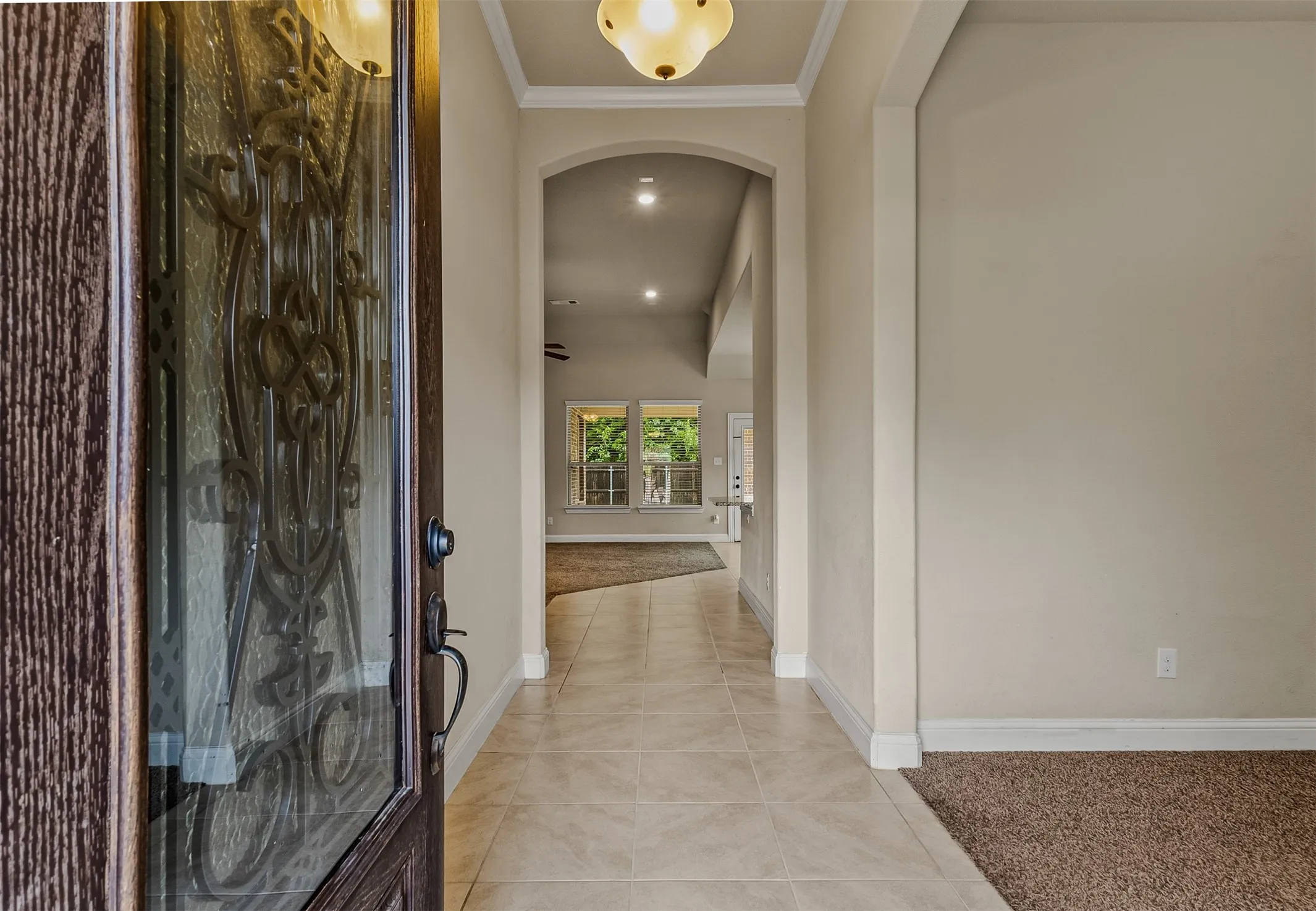 Entryway featuring a decorative glass-paneled door, tile flooring, arched doorway, and crown molding