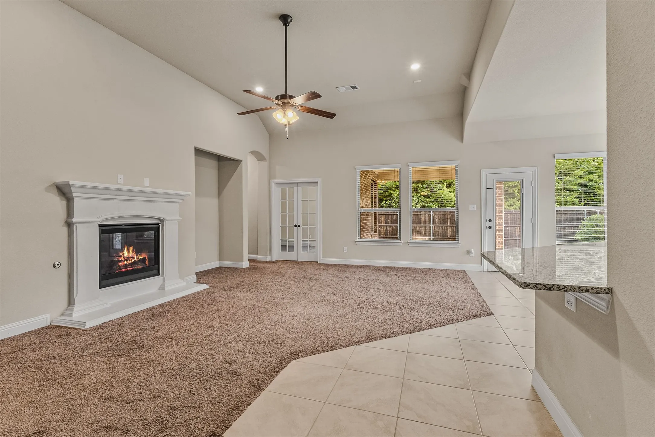 Spacious living area featuring a fireplace with a white mantel, vaulted ceilings, and a ceiling fan