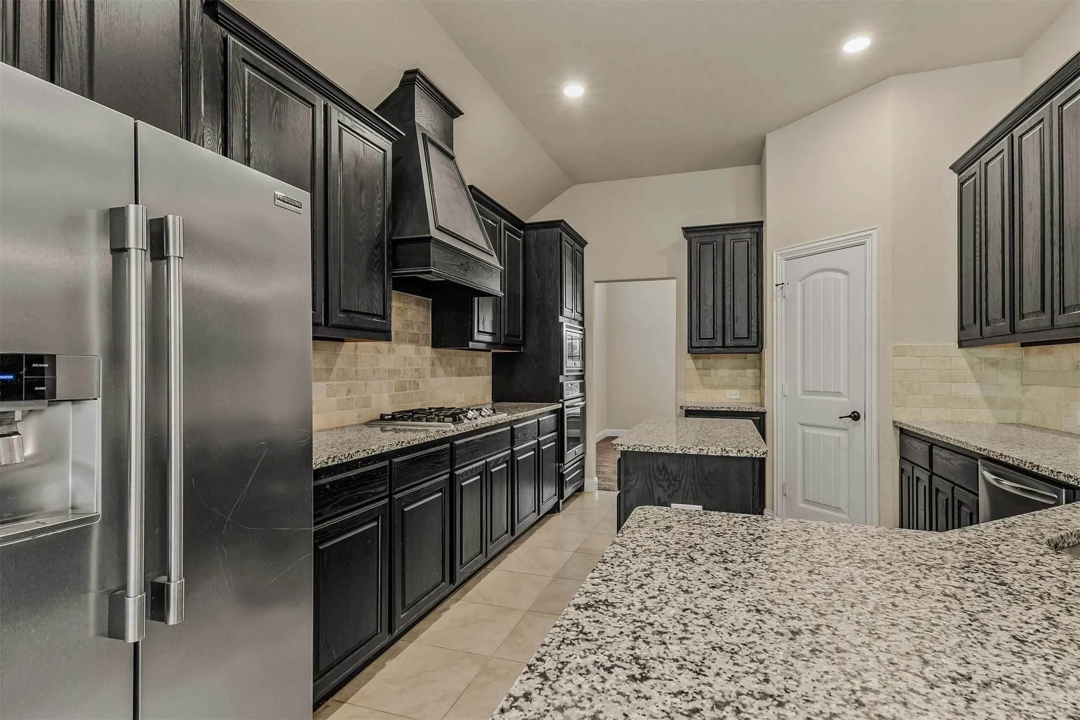 Gourmet kitchen showcasing a stainless steel side-by-side refrigerator, extensive dark wood-finish cabinetry, a gas cooktop, and speckled light-toned countertops