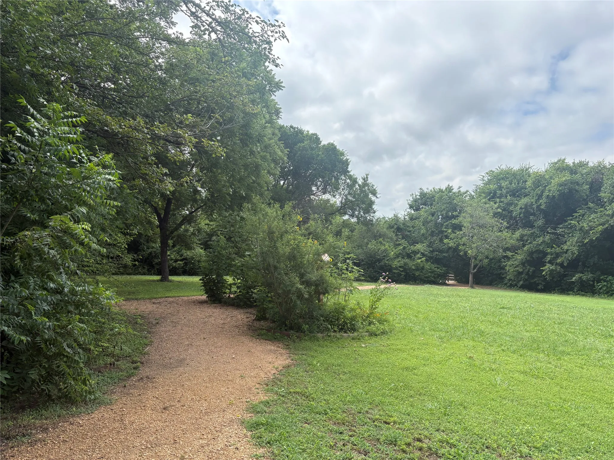 Expansive green space featuring a natural-finish gravel path, mature trees, and dense perimeter foliage. Pettinger Nature Preserve, walking and biking trails.