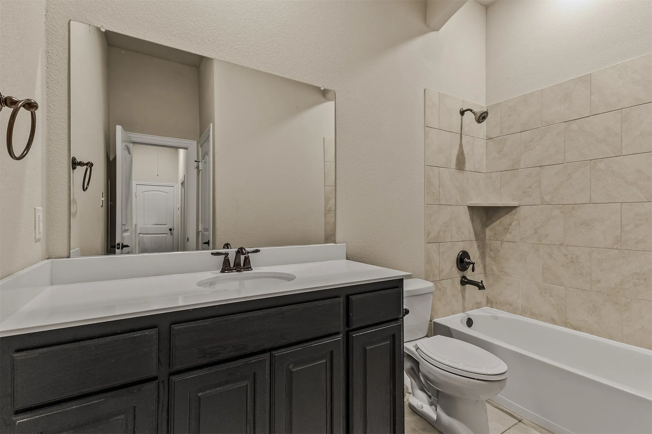 Bathroom featuring a dark wood vanity with a white countertop and integrated sink, bronze-finish fixtures, a tiled bath/shower combination with an integrated niche, and a wall-mounted mirror