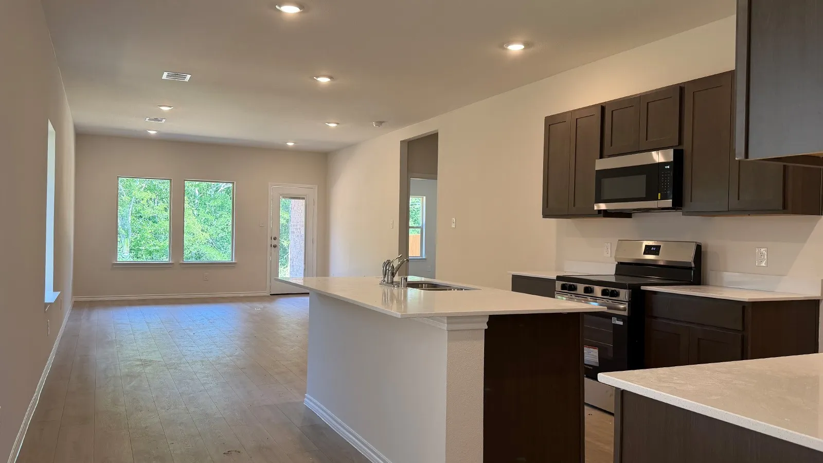 Open-concept living space with wood-finish flooring, recessed lighting, and ample natural light from multiple windows and a glass-paneled door