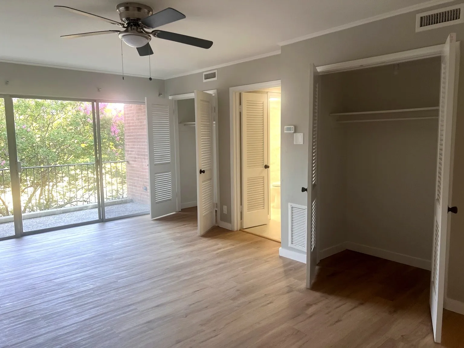 Second bedroom featuring two closets, wood-finish flooring, a ceiling fan with integrated lighting, and a sliding glass door leading to a balcony