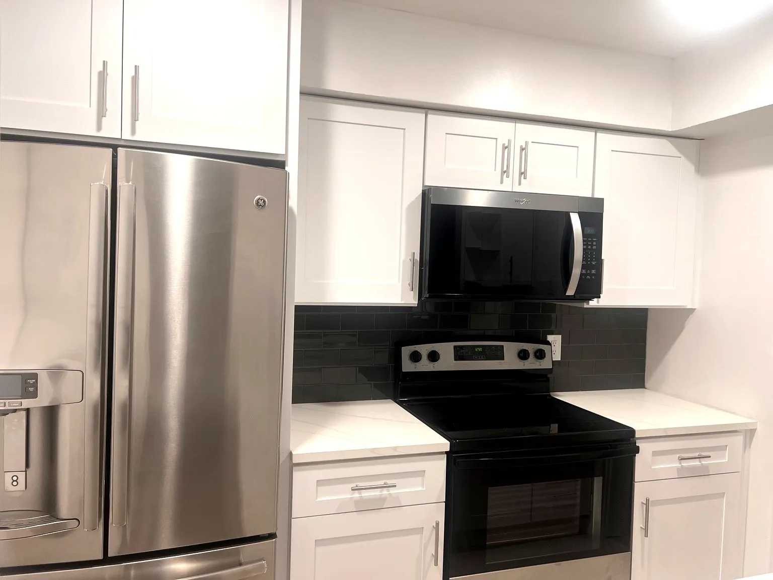 Kitchen featuring white cabinetry, stainless steel appliances, a black subway tile backsplash, and light-colored countertops