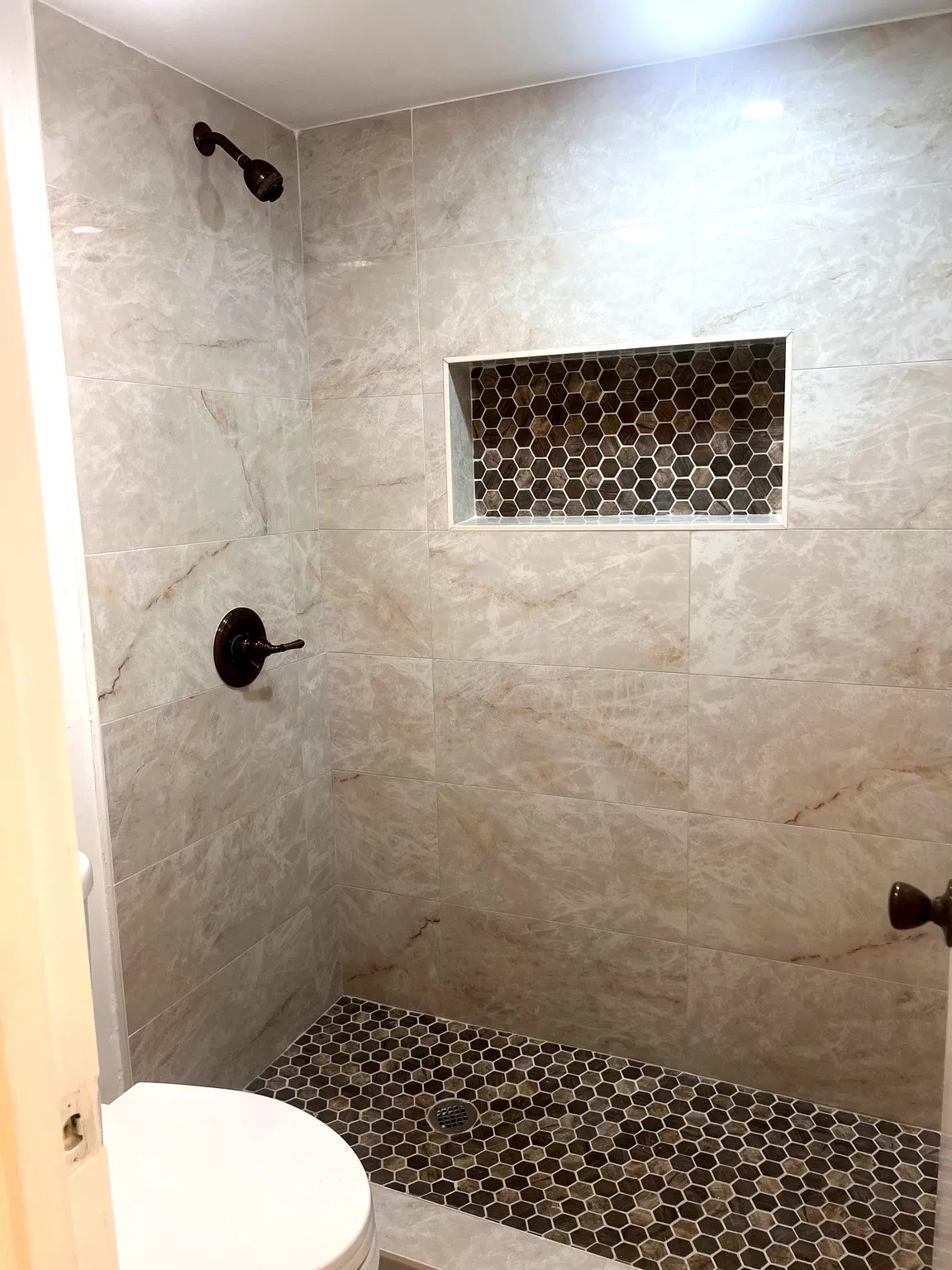 Spacious shower stall featuring large format wall tiles and a multi-tone hexagonal mosaic tile floor