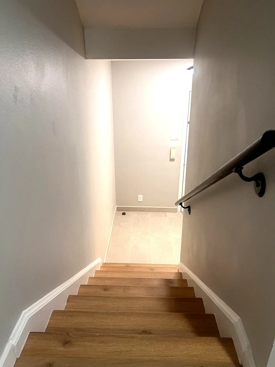Stairwell featuring wood-finish treads, a contrasting white baseboard, a dark wood-finish handrail with black brackets, and light gray wall paint
