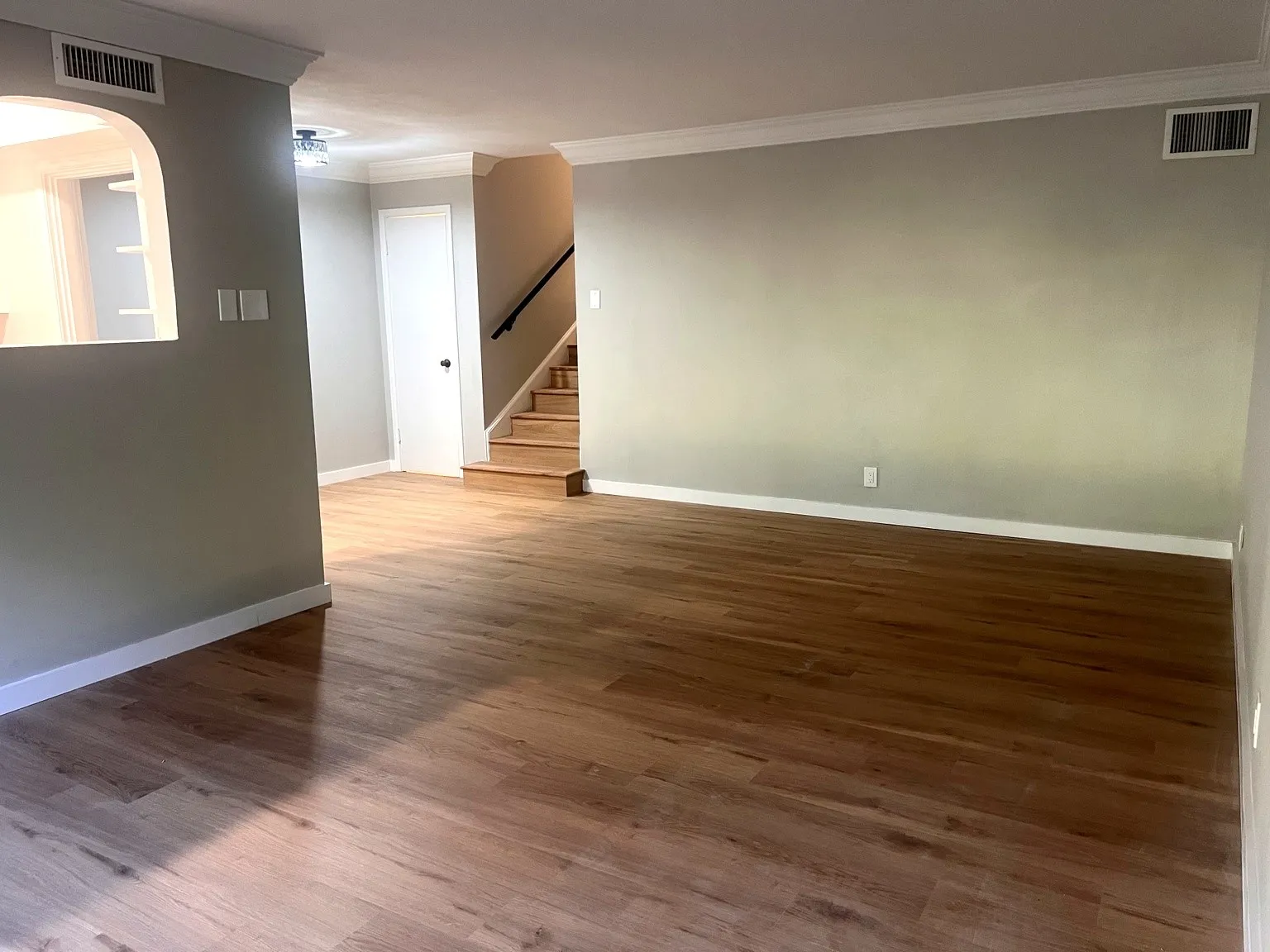 Spacious living room featuring wood-finish flooring, light gray wall paint, and white crown molding.