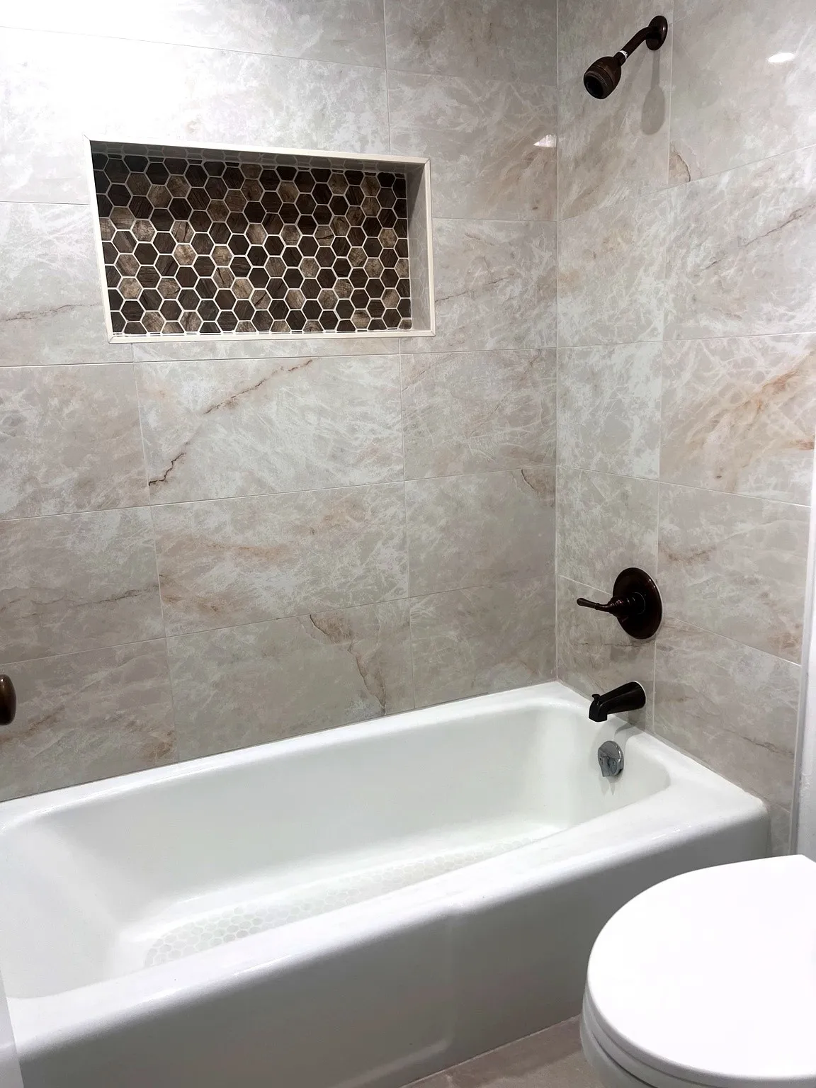 Shower and tub combination featuring marble-look wall tiles, a built-in hexagonal mosaic tile niche, and dark bronze fixtures