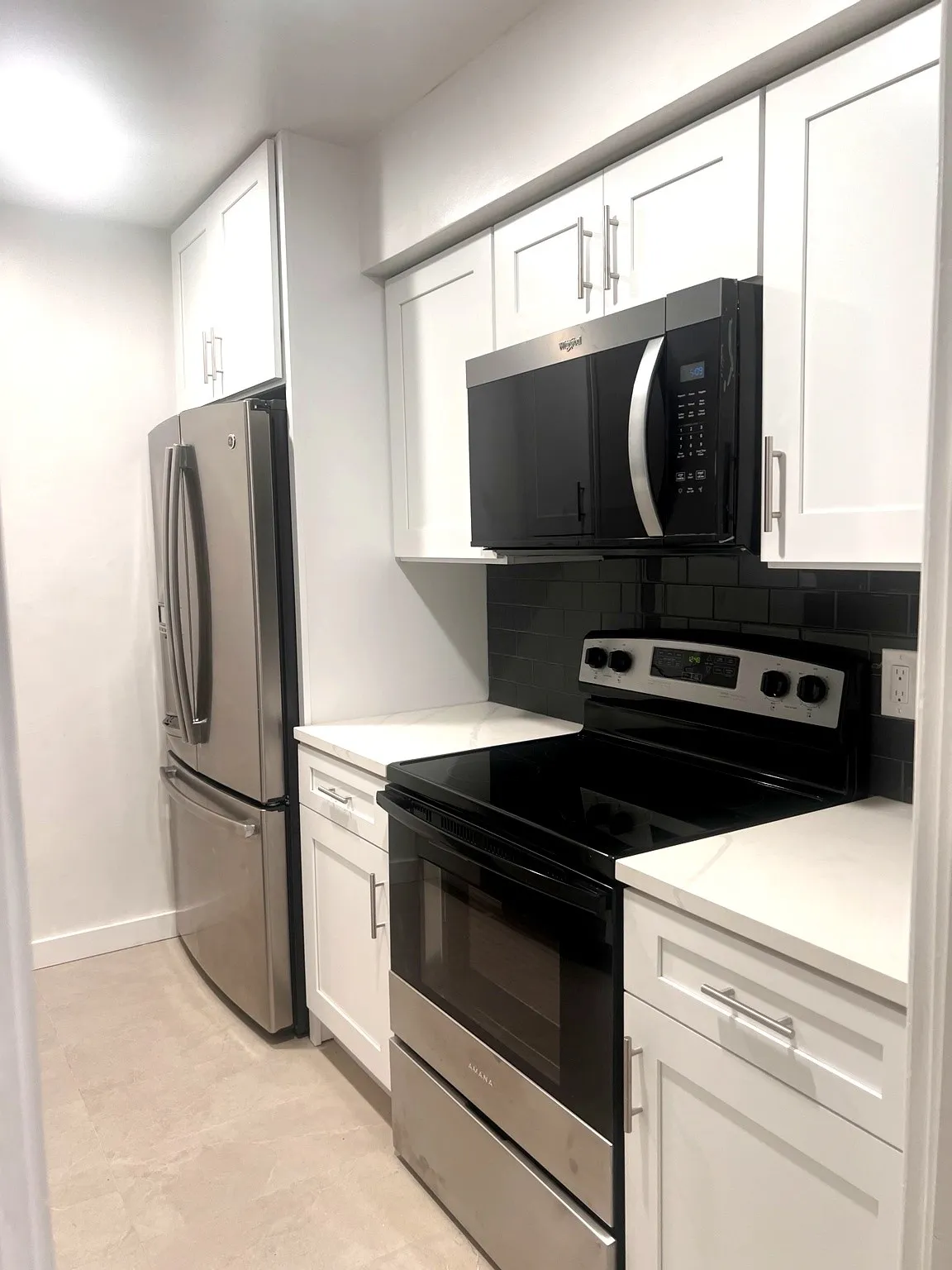 Modern kitchen featuring stainless steel appliances, white shaker-style cabinetry, light-toned countertops, and a dark subway tile backsplash