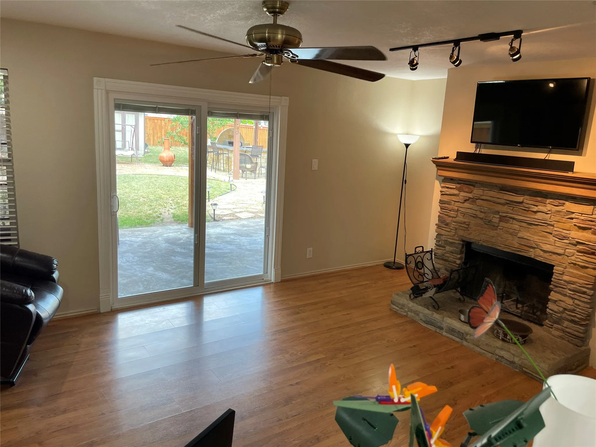 Living room with ceiling fan, rail lighting, a stone fireplace, wood-type flooring, and a textured ceiling