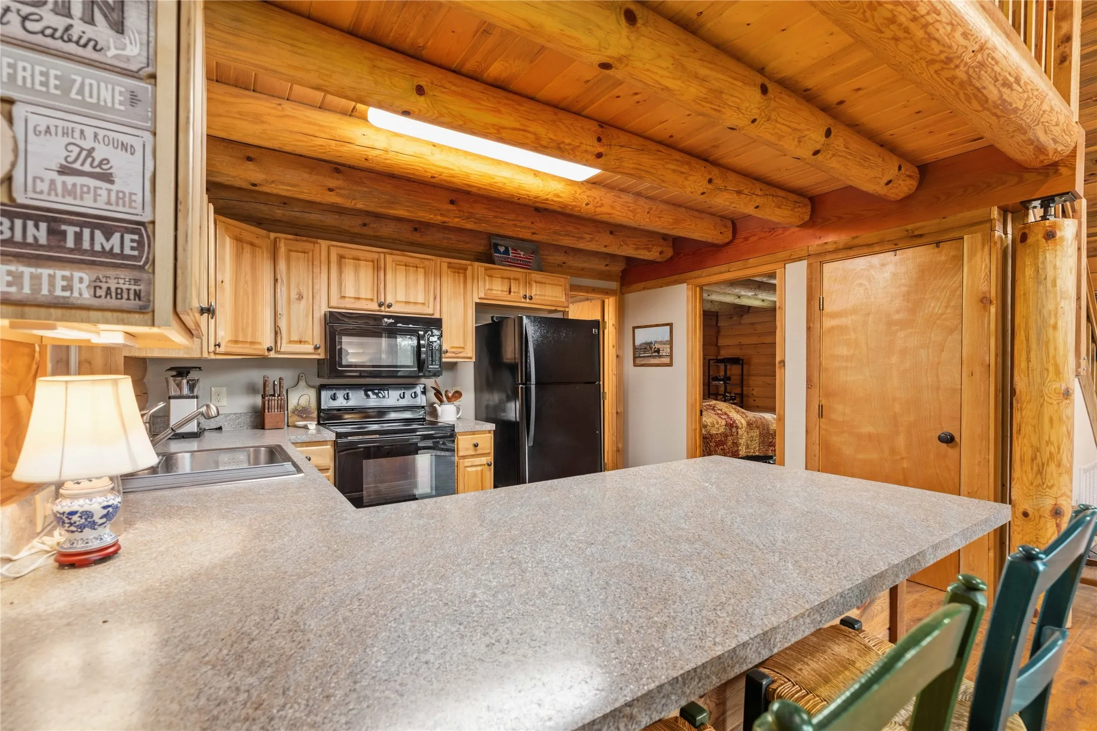 Kitchen featuring log beam ceiling, light wood cabinetry, stone-look countertops, stainless steel sink, and black appliances