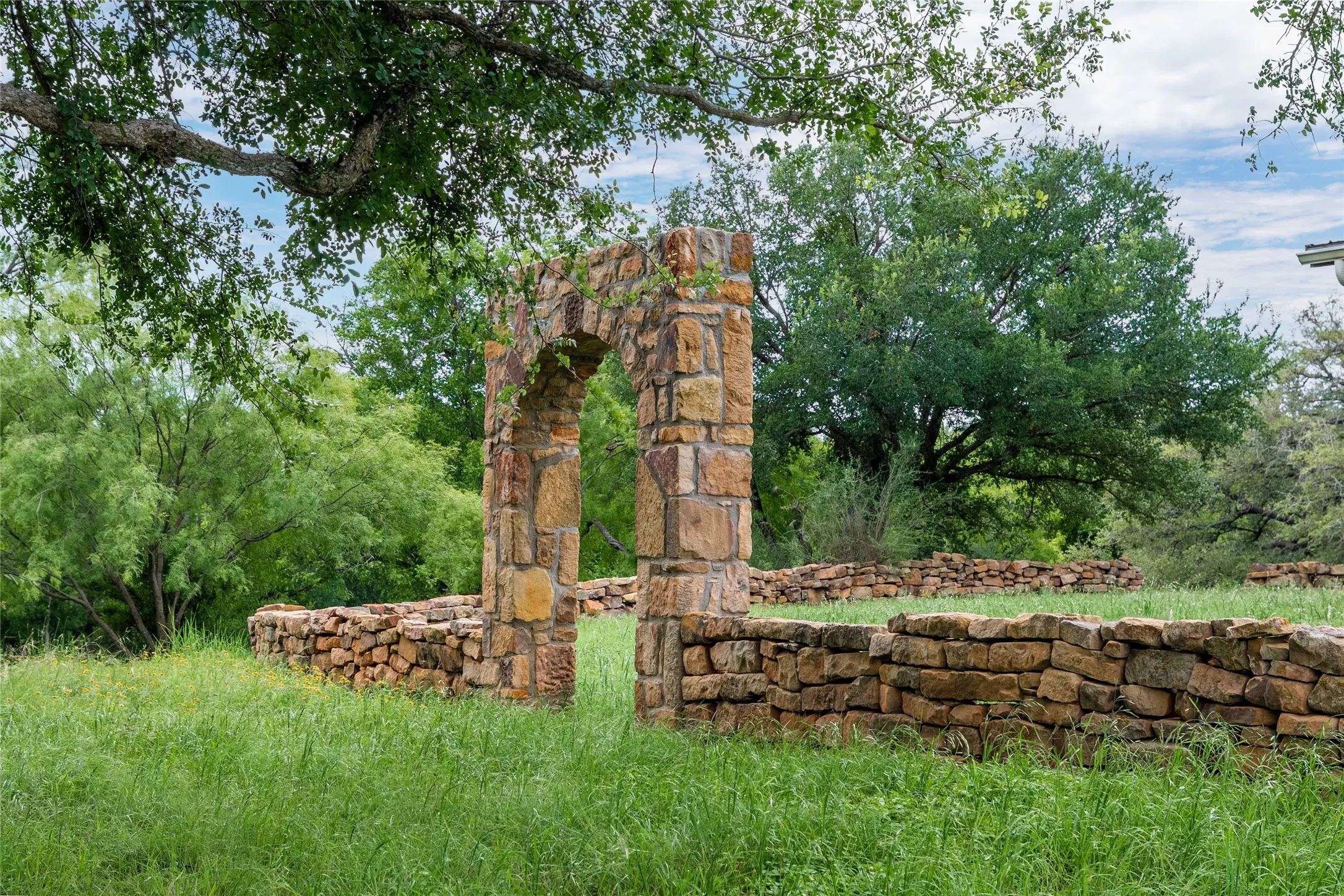 Stone archway feature with natural stone walls, surrounded by abundant green landscaping and mature trees